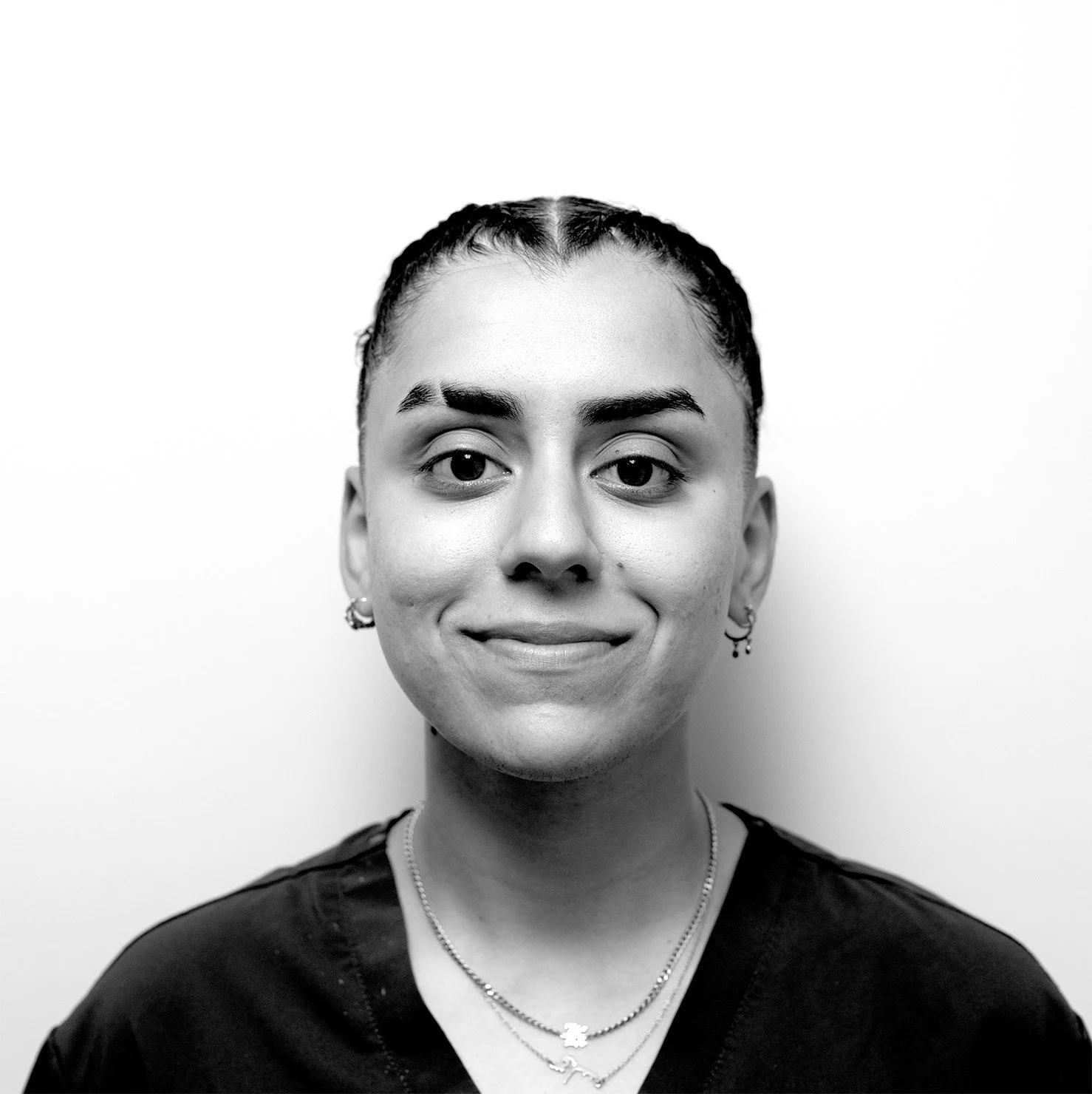 Black and white close-up portrait of a woman with braided hair, earrings, and layered necklaces, smiling slightly against a plain white background.