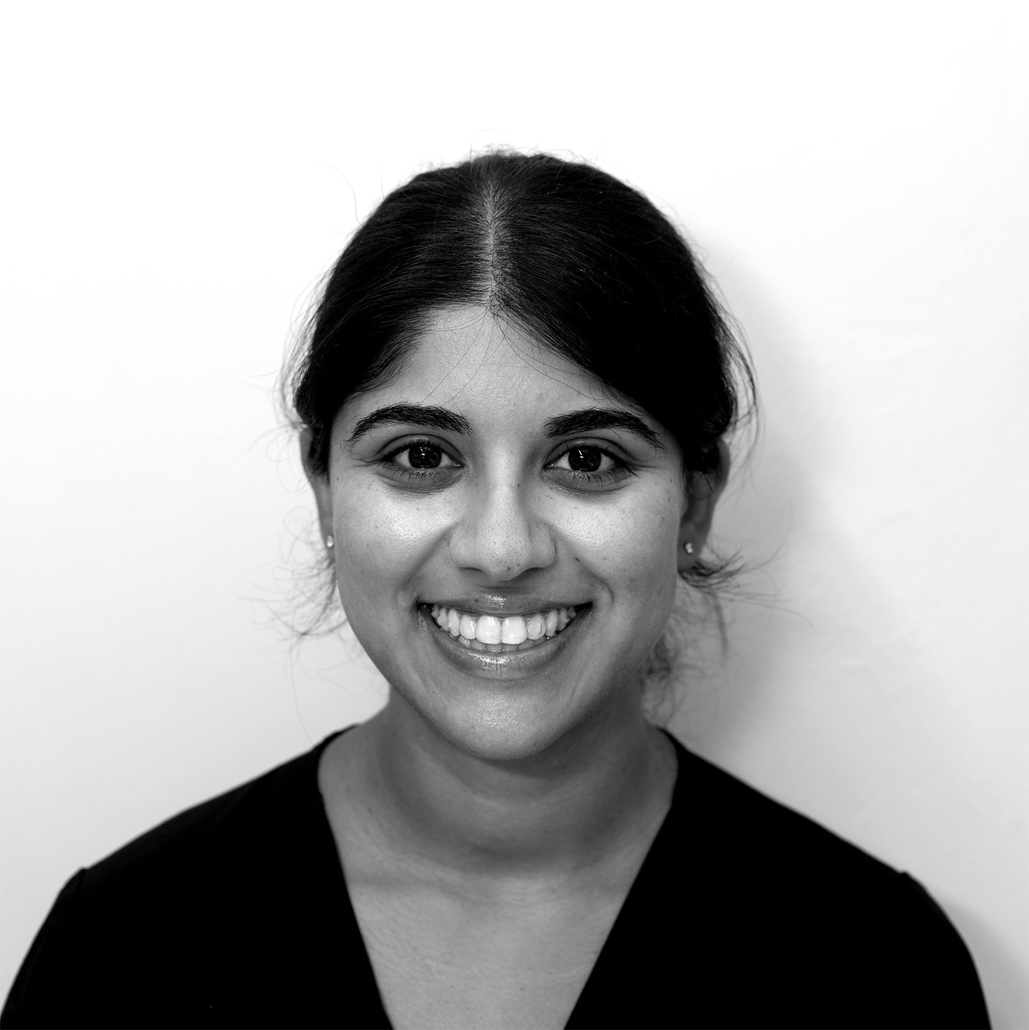 Black and white portrait of a smiling woman with dark hair, wearing a dark top, against a plain light background.