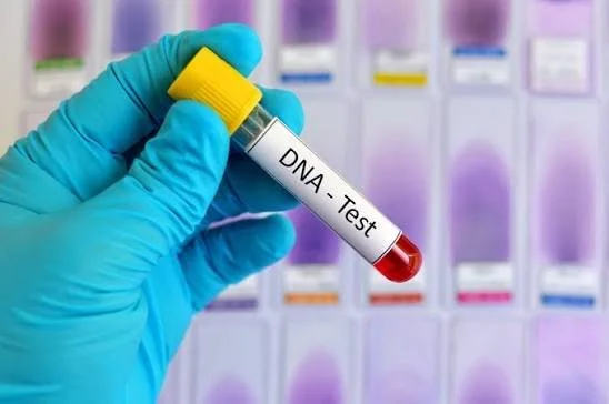 A gloved hand holding a blood sample labeled 'DNA Test' in front of a lab background with test tubes.