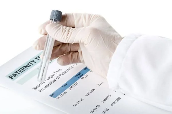 A person wearing a white medical glove holding a pen over a paternity test report