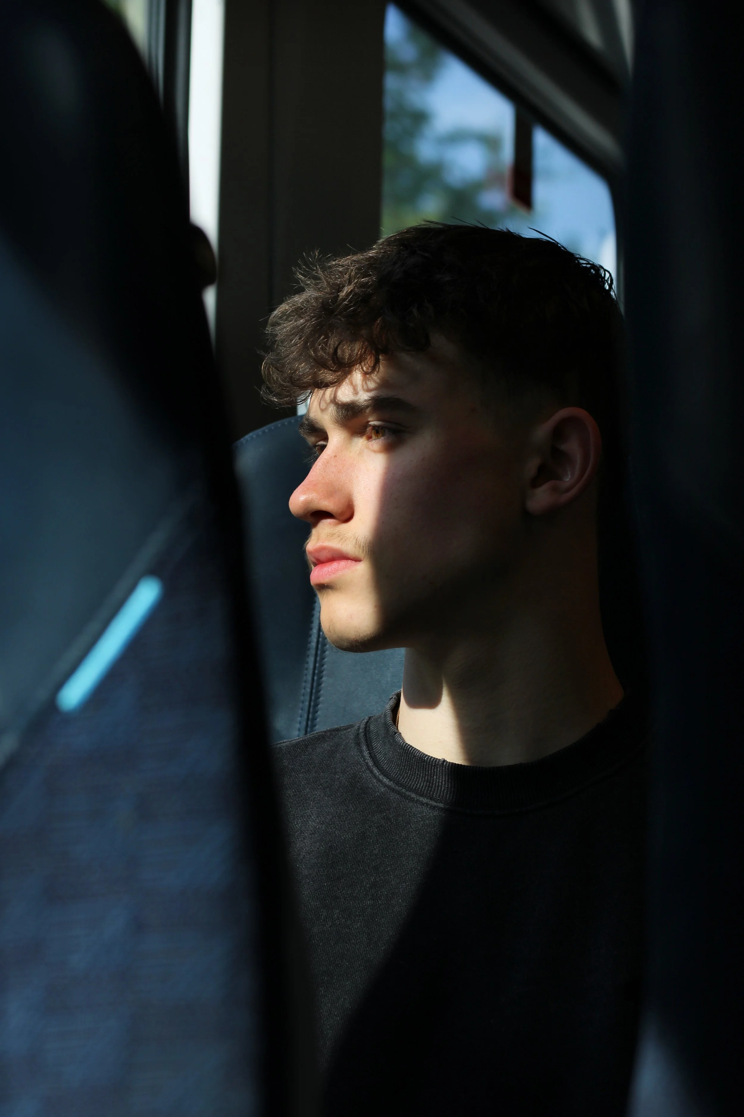 A young man looking wistfully out of a train window in Surrey. Sun is shining on part of his face. Photographer: Blake Charles.