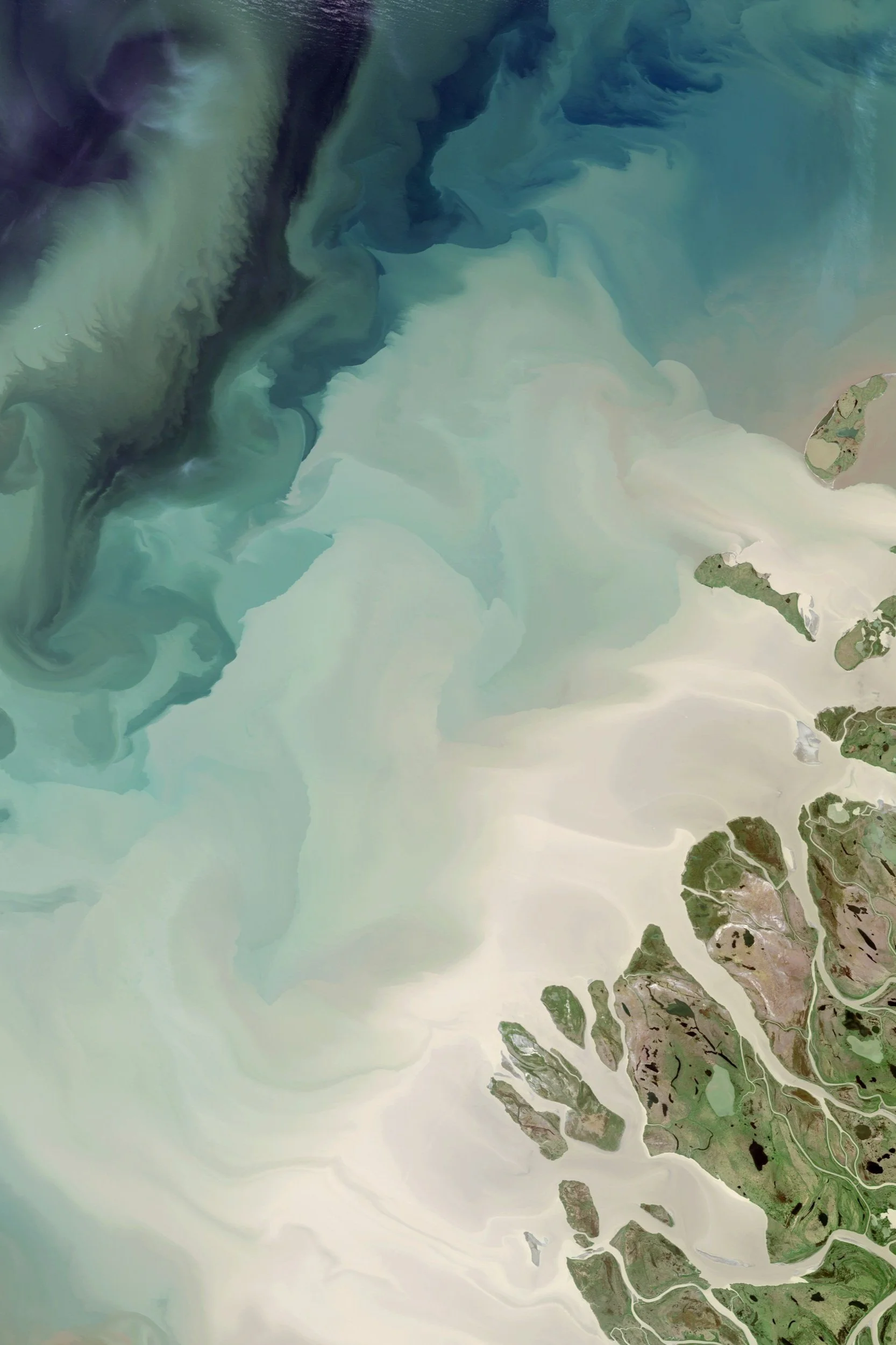 A satellite image showing the coastline with sandy beaches, green land, and blue water in shades of turquoise and deep blue.