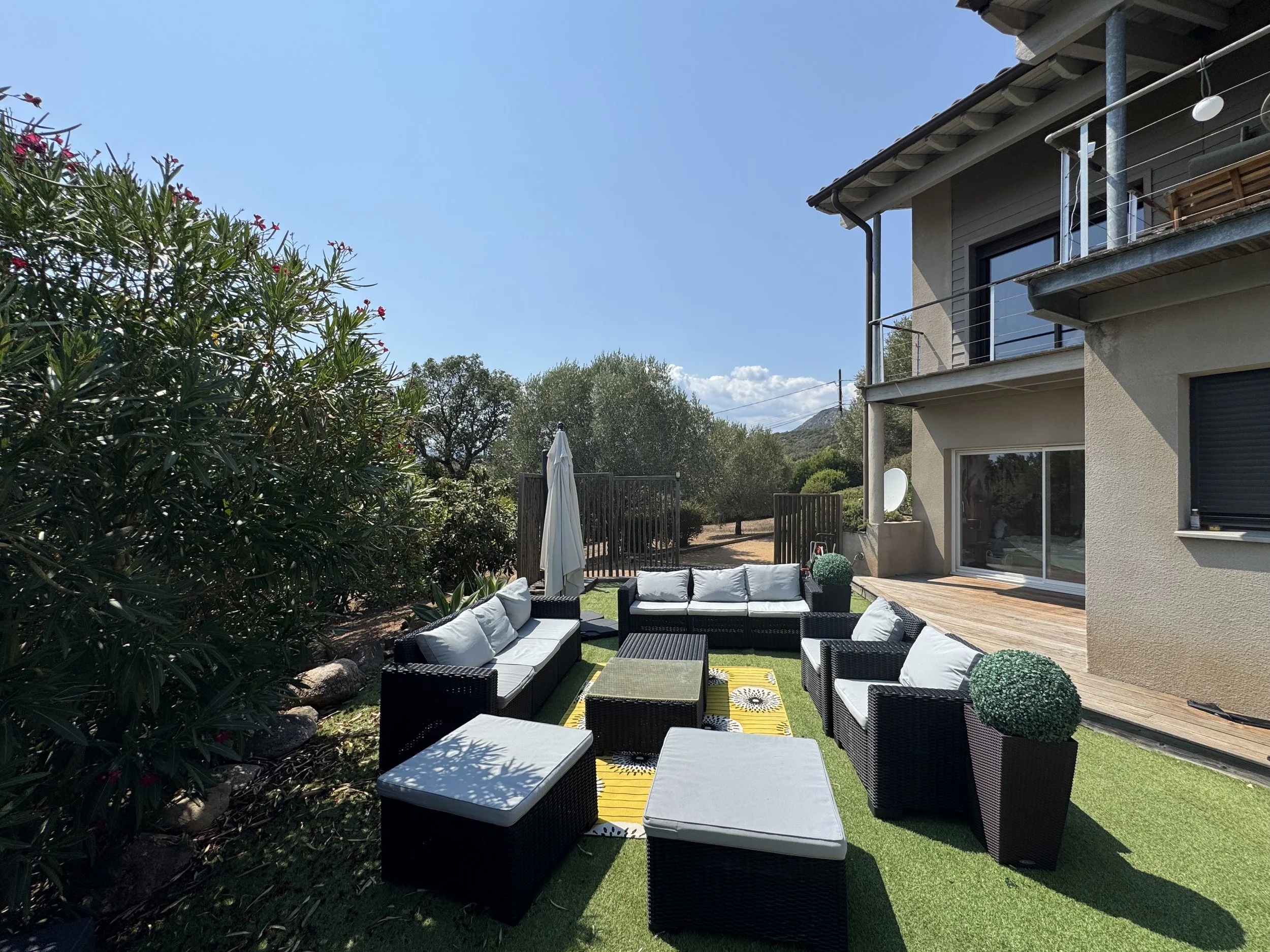 salon de jardin en résine tréssée, avec parasol, entre la piscine et le terrain de pétanque.