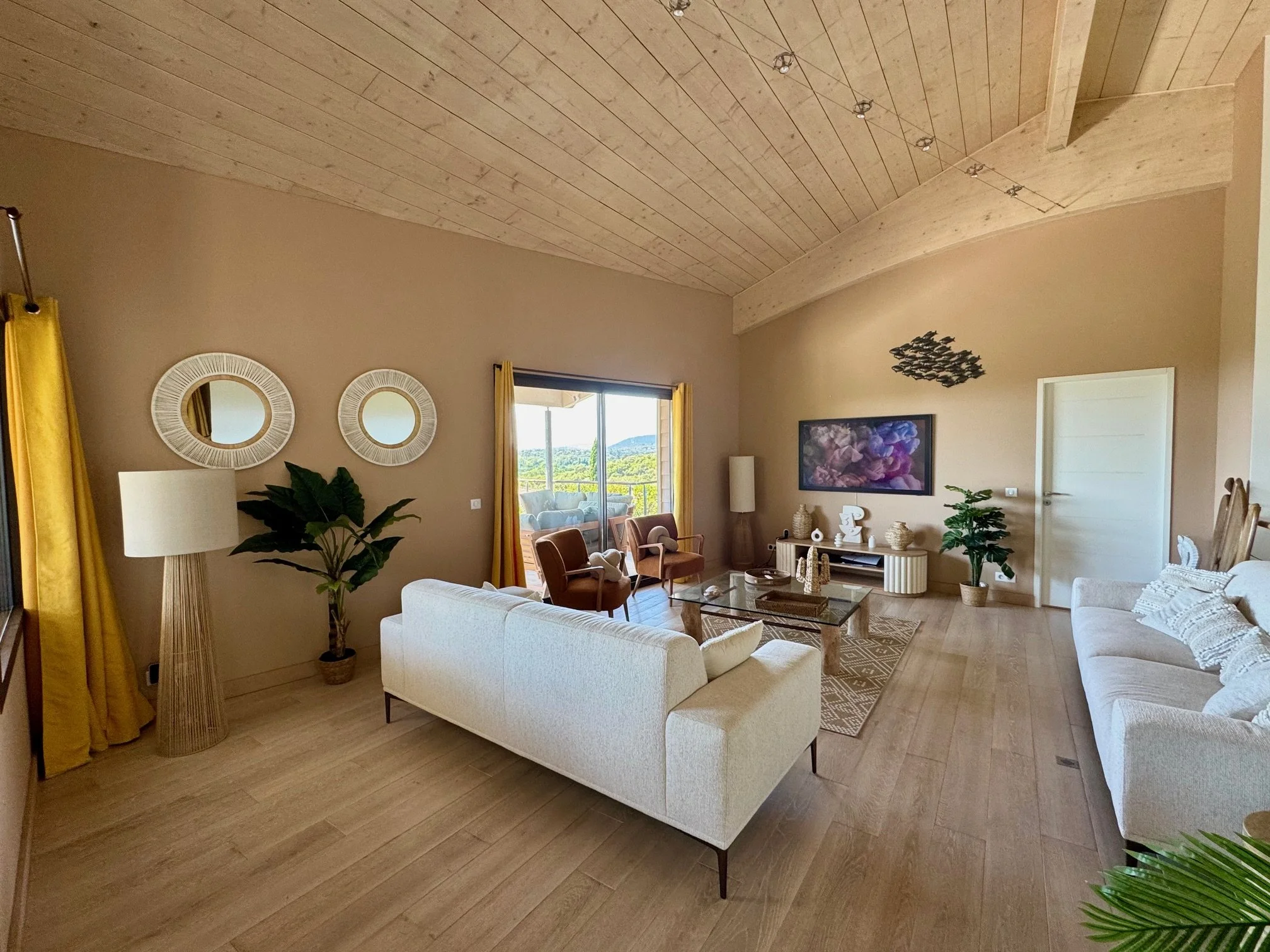 Salon moderne avec deux canapés blancs, deux fauteuils en cuir marron, un téléviseur mural,une porte-fenêtre donnant sur une terrasse avec vue sur la mer.