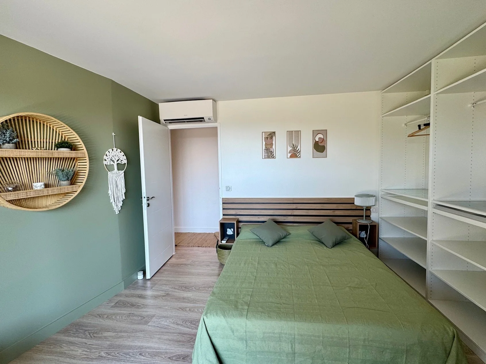Chambre Selena, lit 160 avec tête de lit en bois,
grande fenêtre  coulissante donnant sur le jardin et la piscine, étagères murales en bois, et un lampadaire en bois.