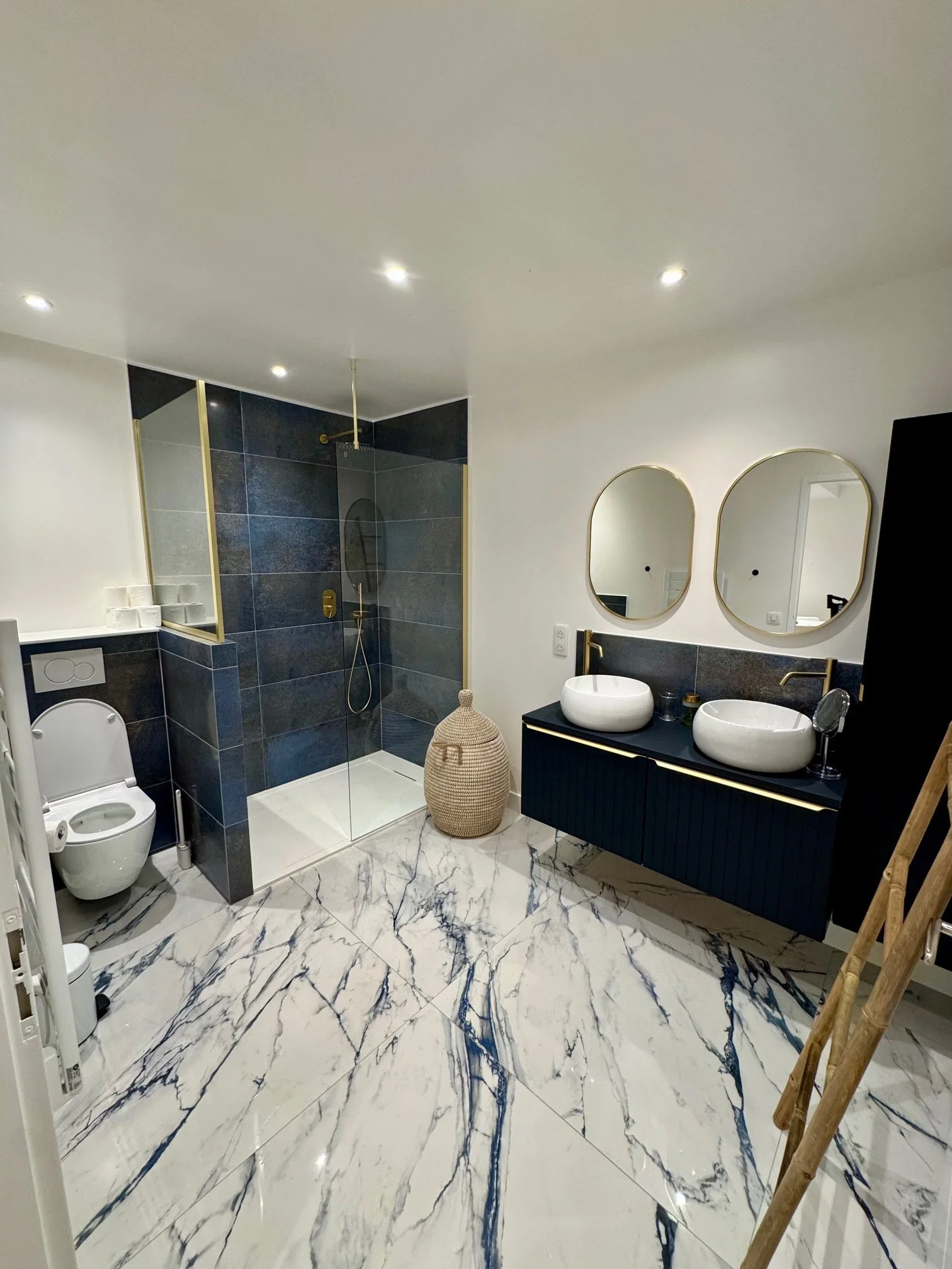 Salle de bain moderne avec meuble lavabo double vasque, WC, douche à l'italienne, sol en marbre bleu et blanc.