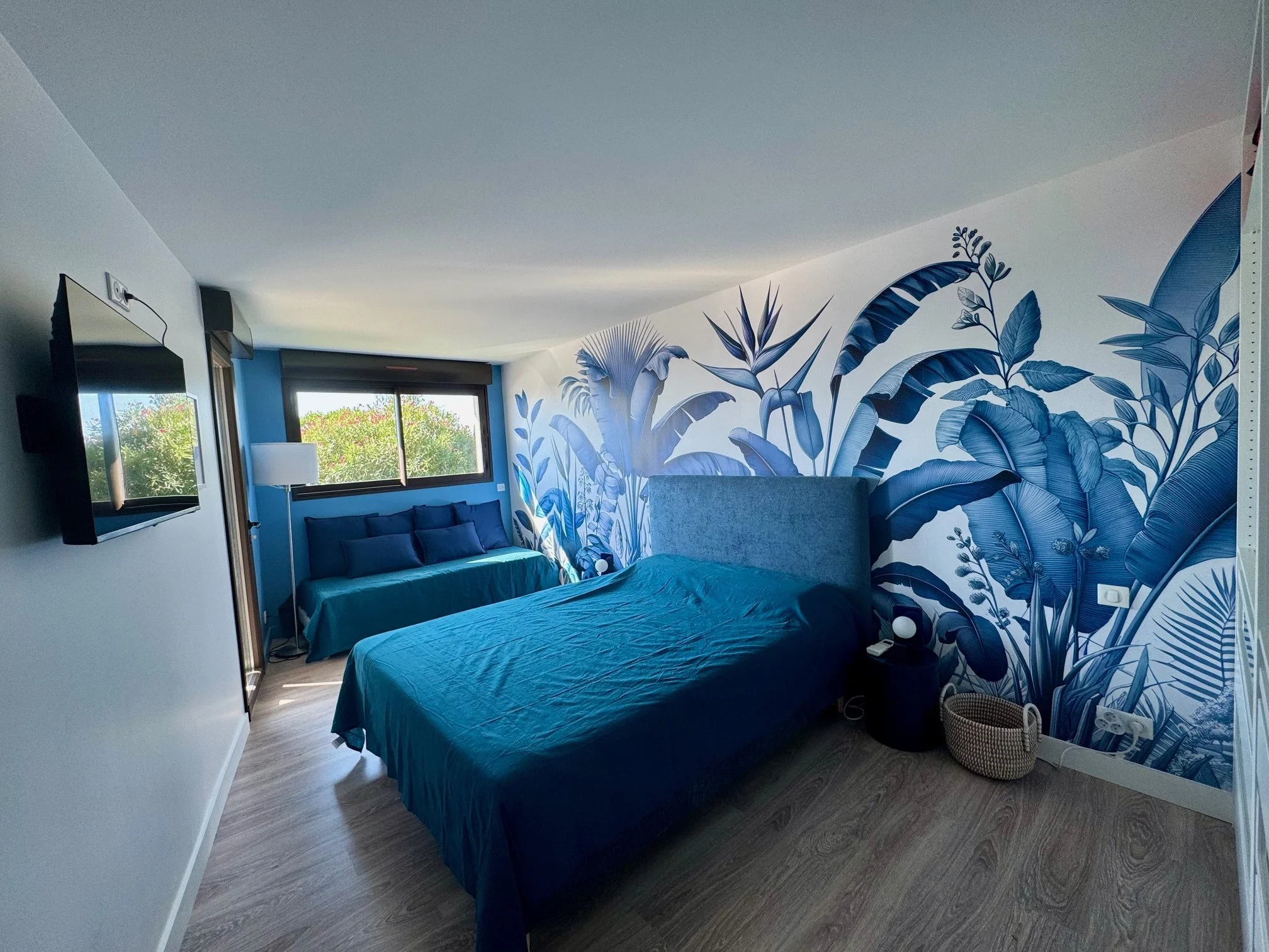 Chambre Tessa, lit 160 avec tête de lit , fenêtre large avec vue sur la nature, petite banquette bleue, télévision murale.
