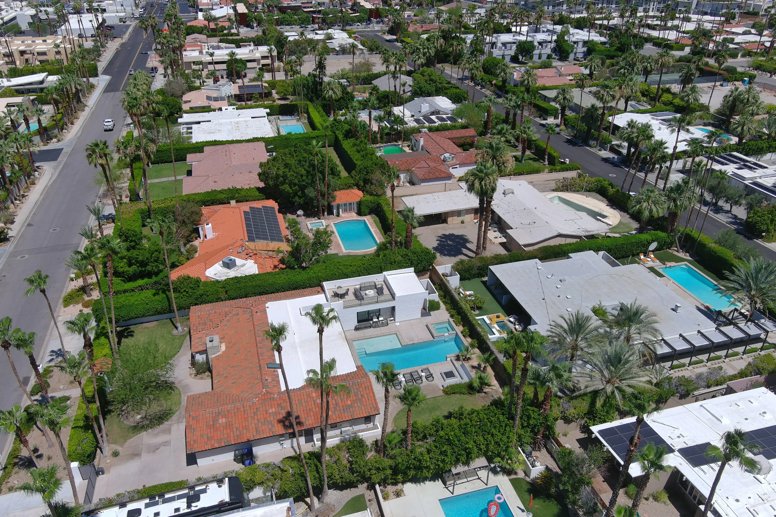 Aerial view of a residential neighborhood with houses, swimming pools, palm trees, and green lawns.