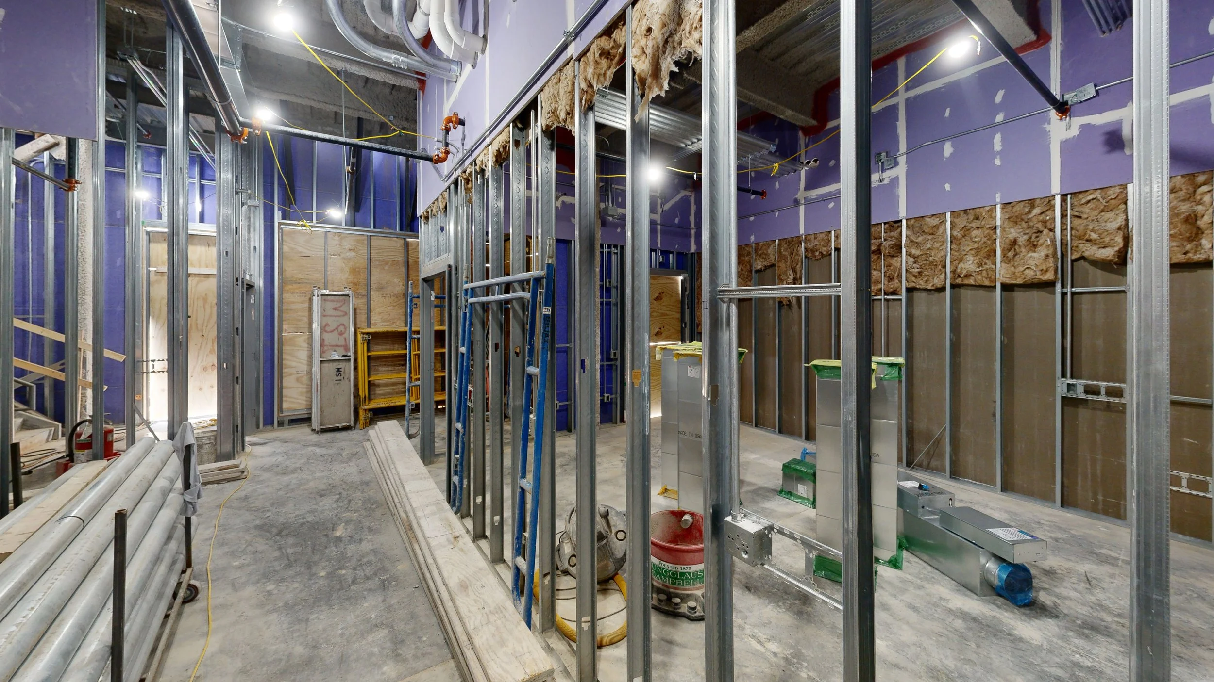 Interior of a building under construction with metal framing, insulation, and various construction tools and materials.