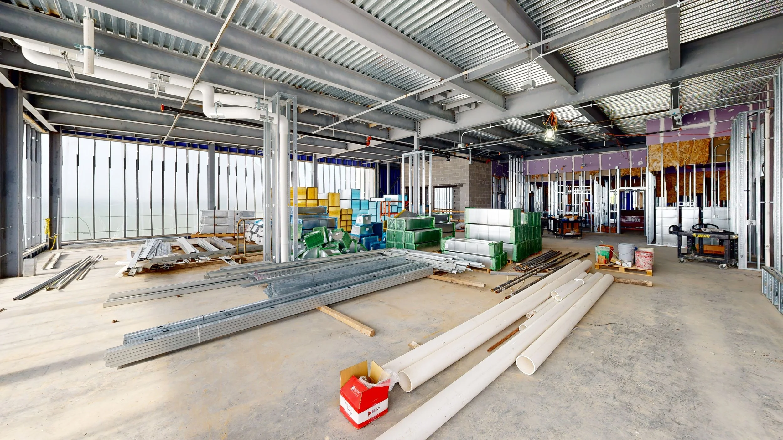 Construction site with metal framing, pipes, and building materials inside a partially built structure.