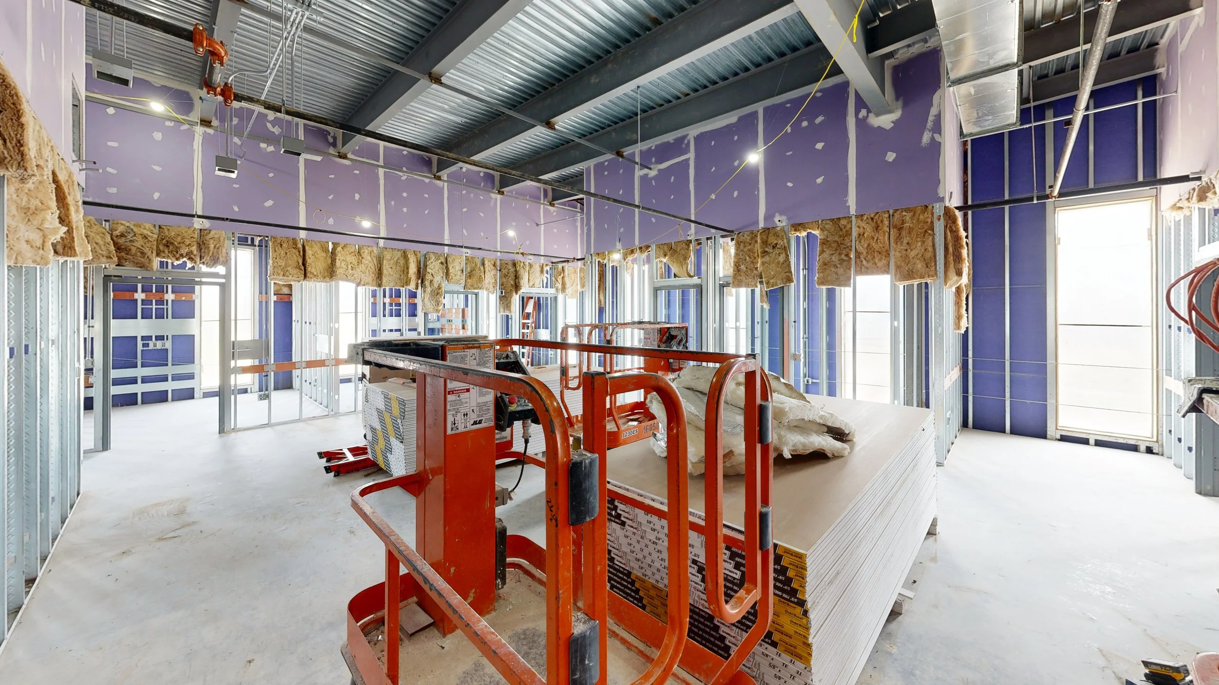 Interior of a building under construction with exposed framing, insulation, and drywall installation in progress.