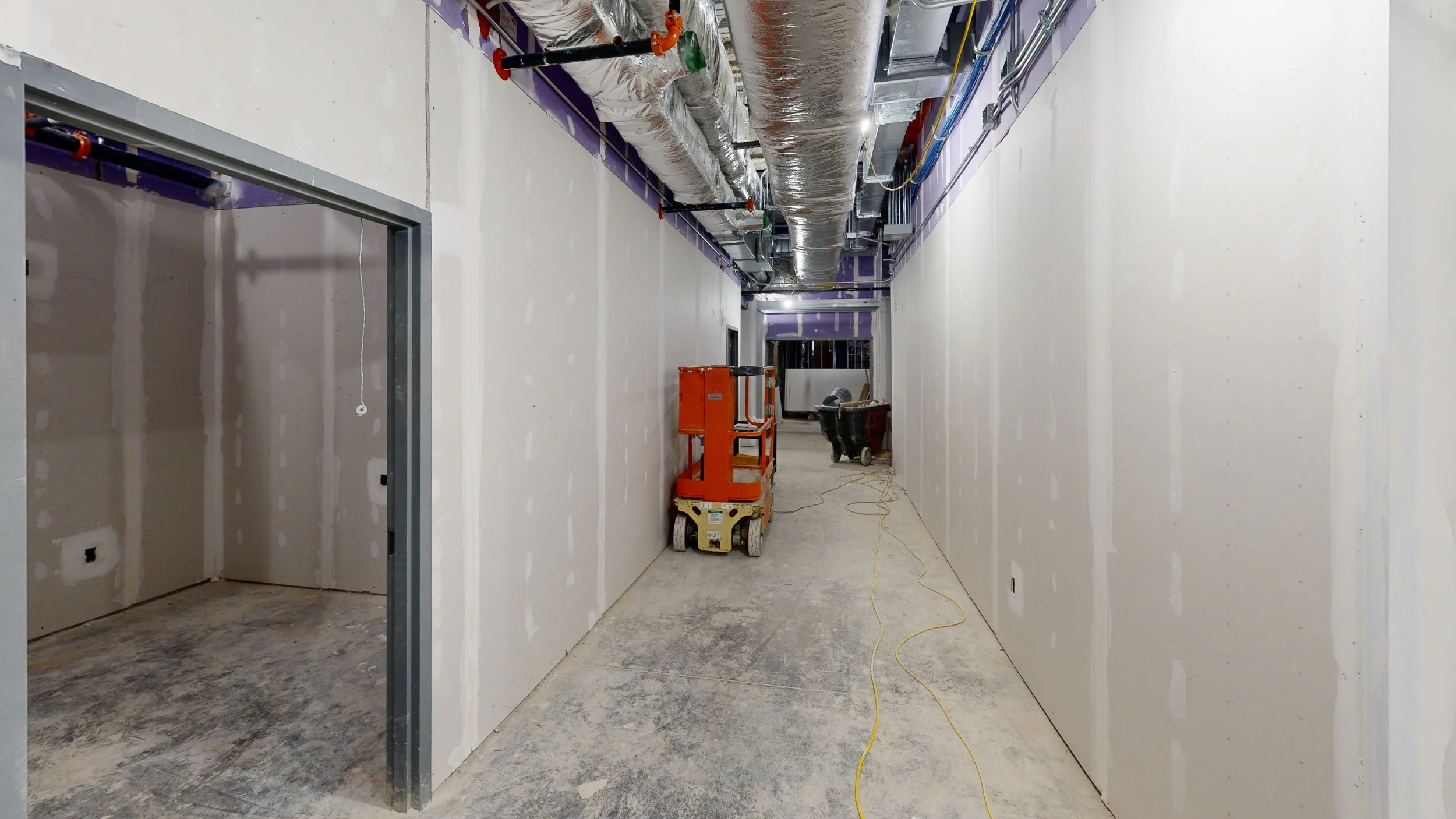 Construction hallway with drywall walls, ceiling ductwork, and construction equipment.