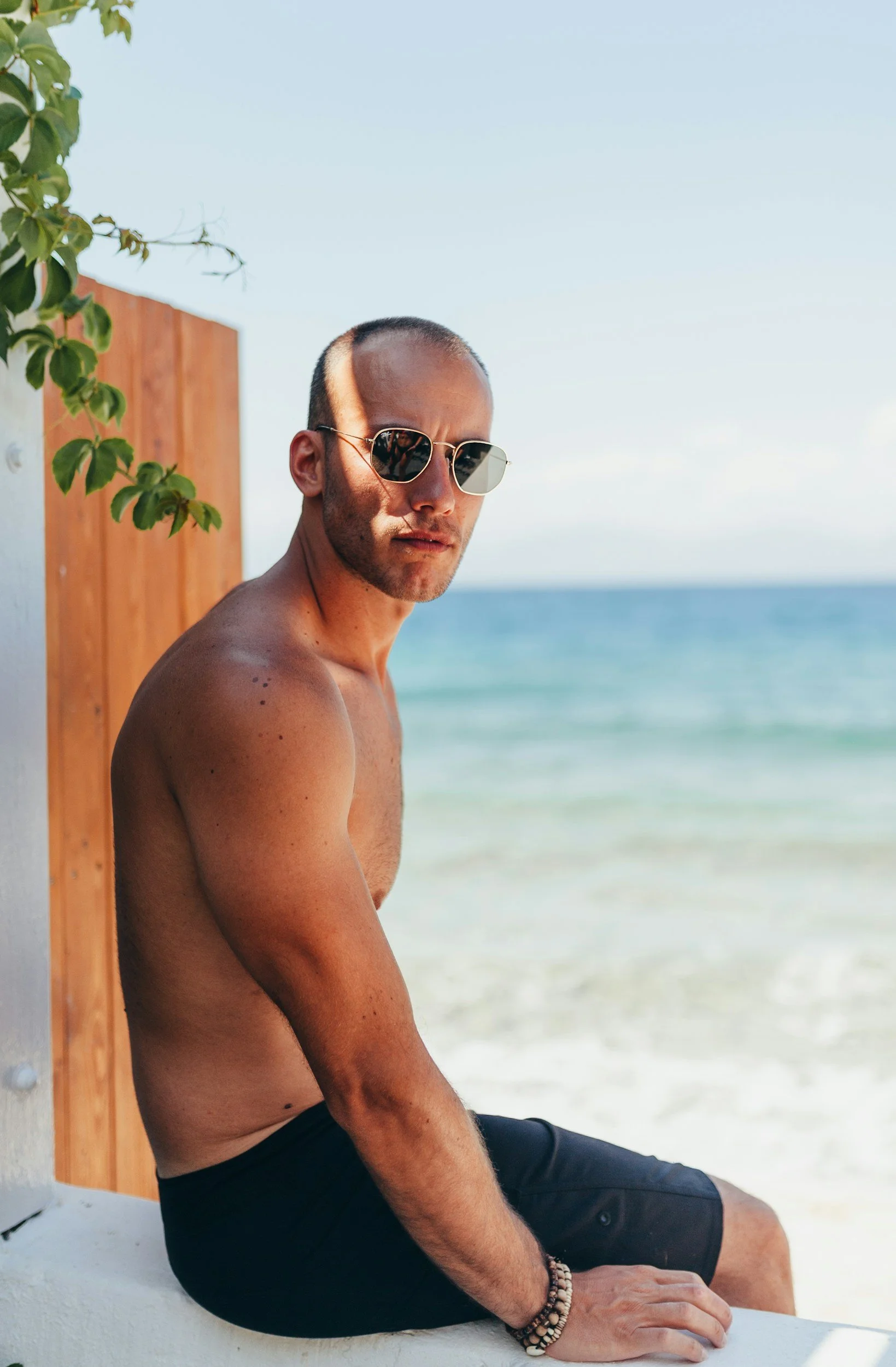 A shirtless man wearing sunglasses and black shorts