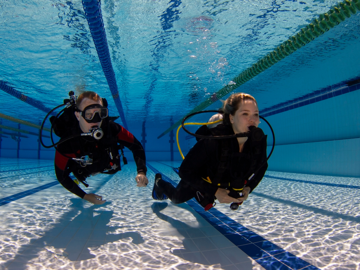 Two scuba divers in a swimming pool practicing underwater breathing exercises.