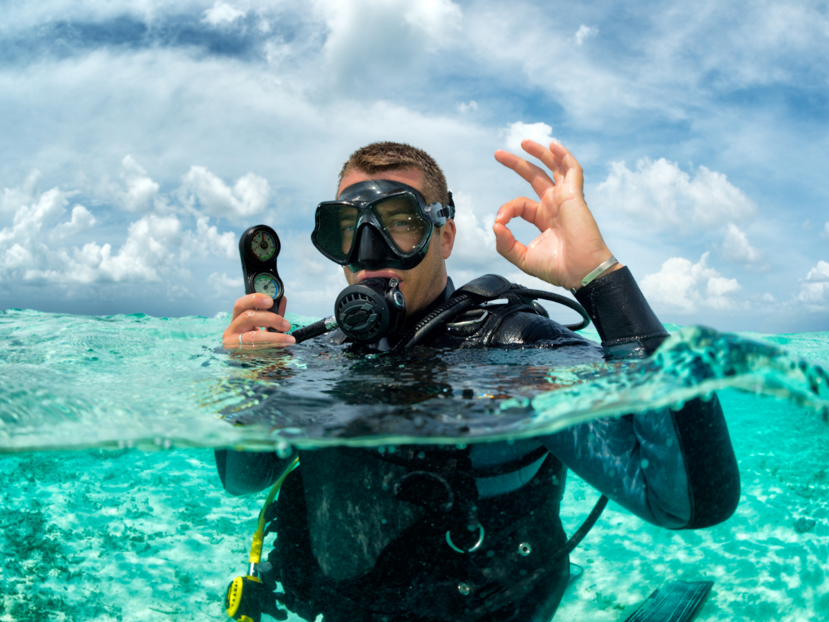 A scuba diver in the ocean holding a compass and making an OK hand gesture.