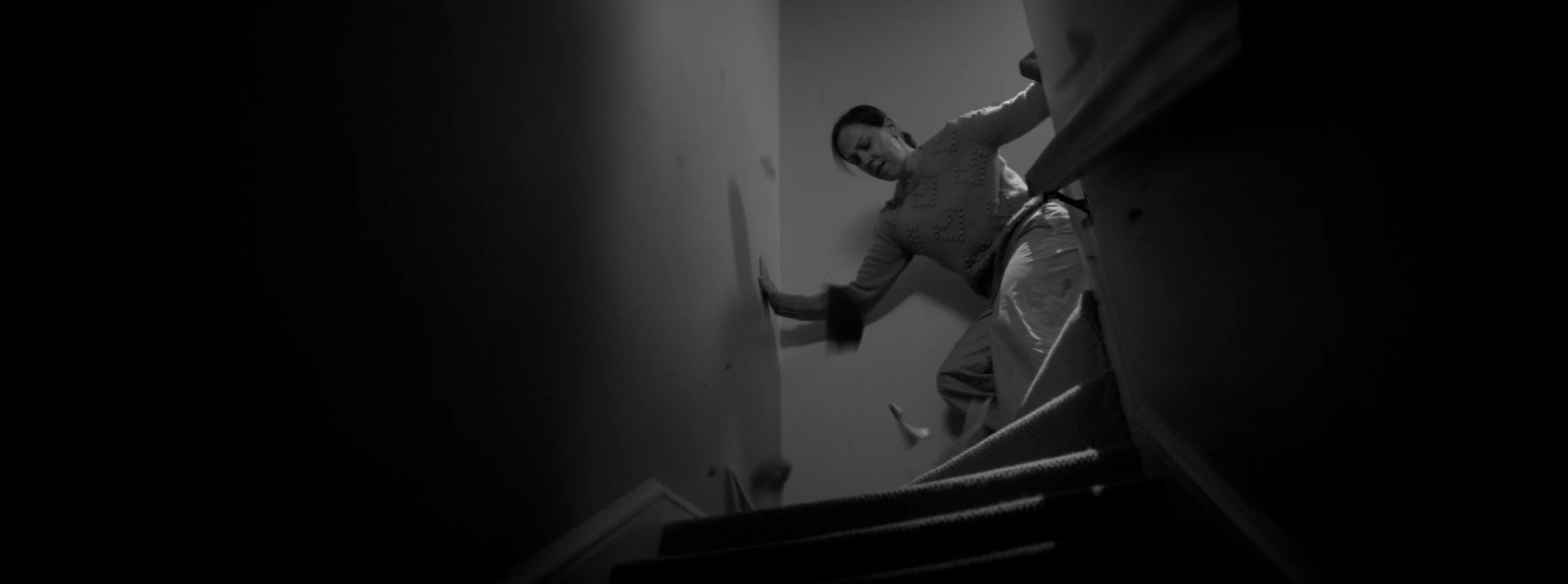 A woman in pajamas is falling down the stairs, caught mid-fall, in a dimly lit staircase.