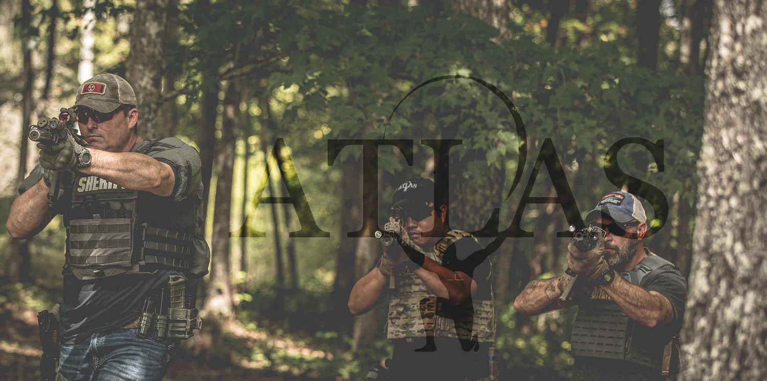 Three men in tactical gear aiming rifles in a forested area during daytime.
