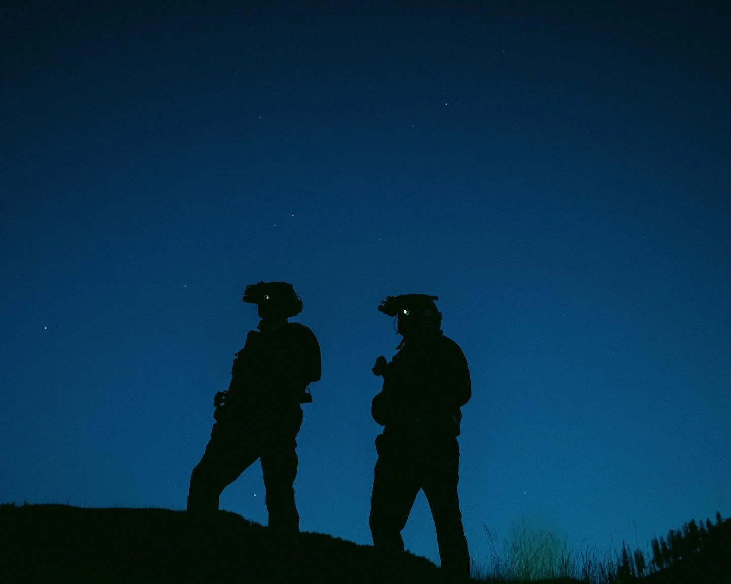 Silhouette of two soldiers standing on a hill under a starry night sky.
