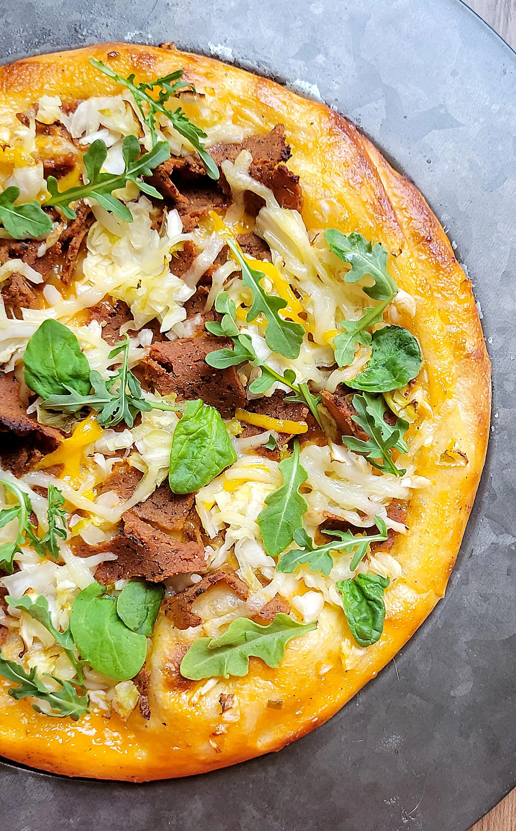 Close-up of a freshly baked dairy-free Reuben pizza topped with vegan Corn’d Beef, shredded sauerkraut, melted dairy-free cheese, and fresh arugula on a golden crust.