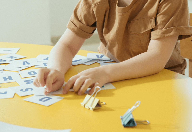 child in brown shirt playing with letters on a yellow table