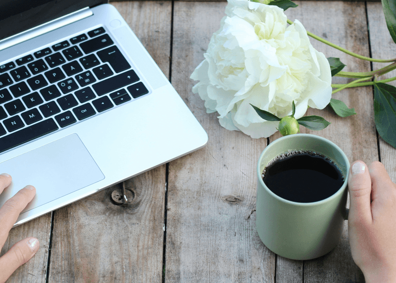 laptop green coffee mug and white flowers on wooden table
