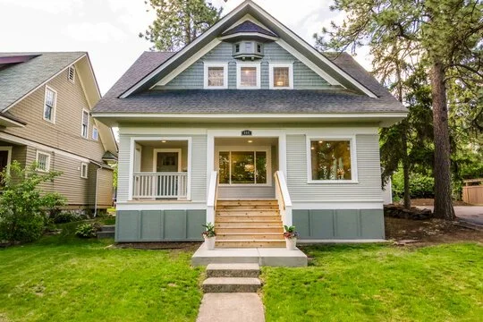 Front view of a two-story house with a front porch, steps, and a well-maintained lawn, surrounded by trees.