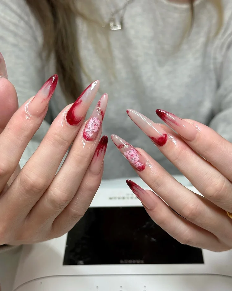 Iris nail art: Long pointed nails with a red and pink marble design