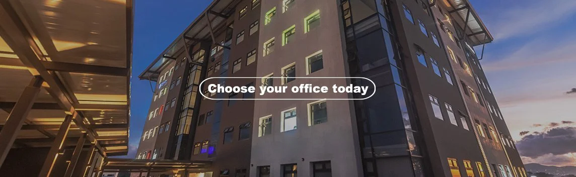 Modern corporate building at sunset with illuminated windows and a central banner that reads 'Choose your office today'