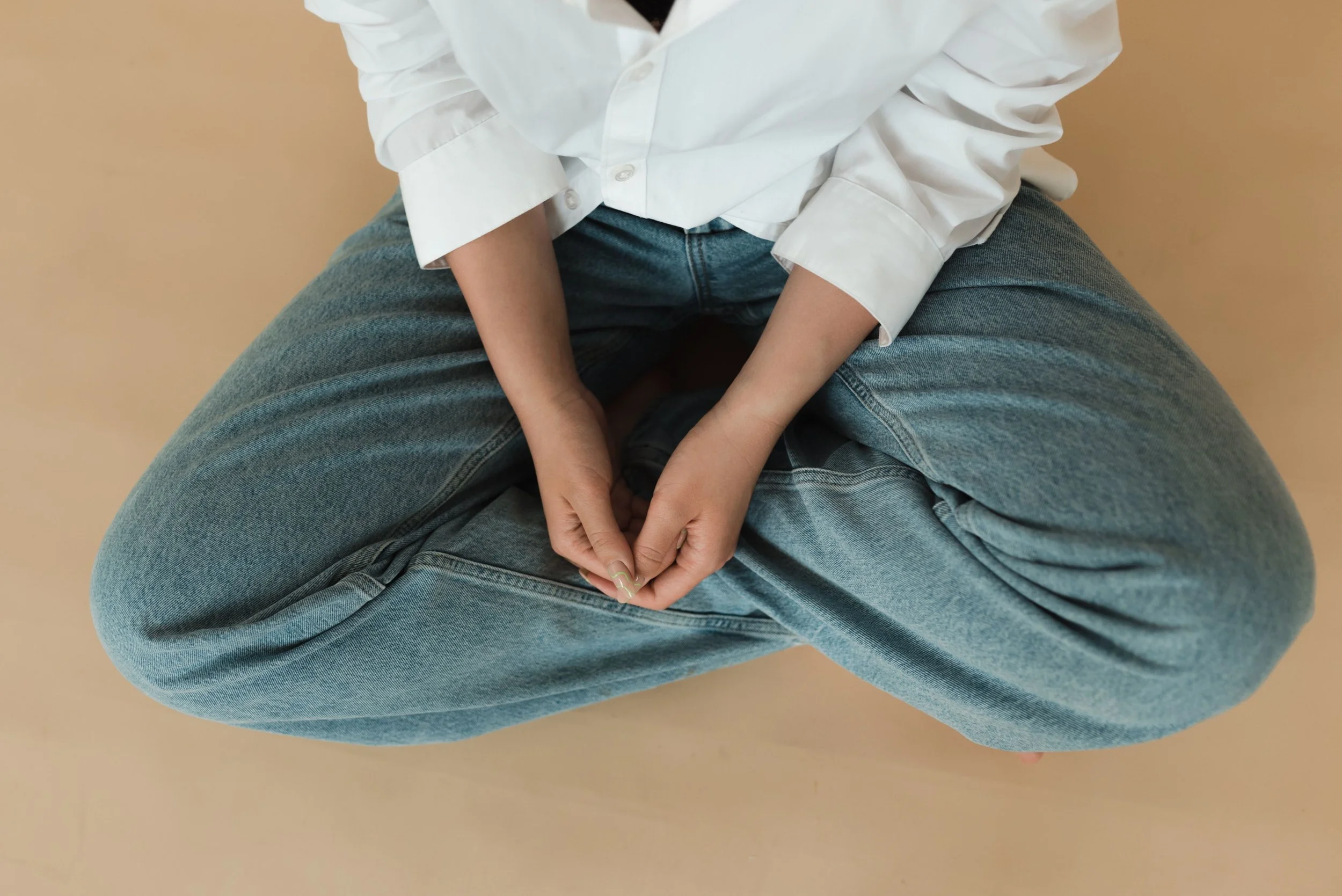 A woman sits cross-legged on the floor with her hands resting open in her lap, a posture of grounded attention often present in somatic and attachment-focused EMDR work.