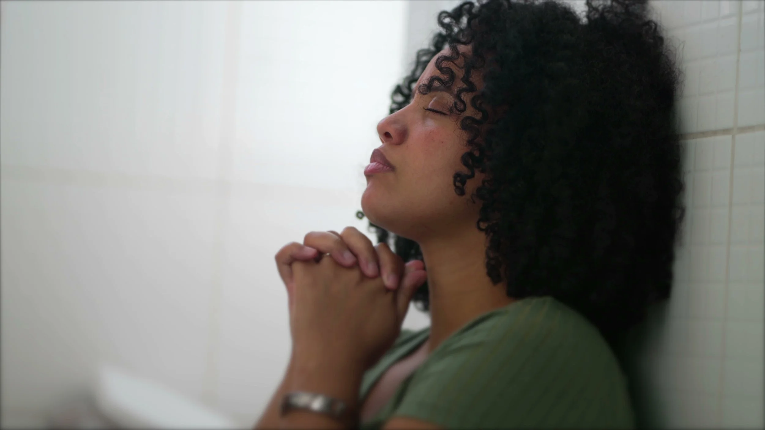 Person practicing mindfulness reflection while clasping hands, and closed eyes.