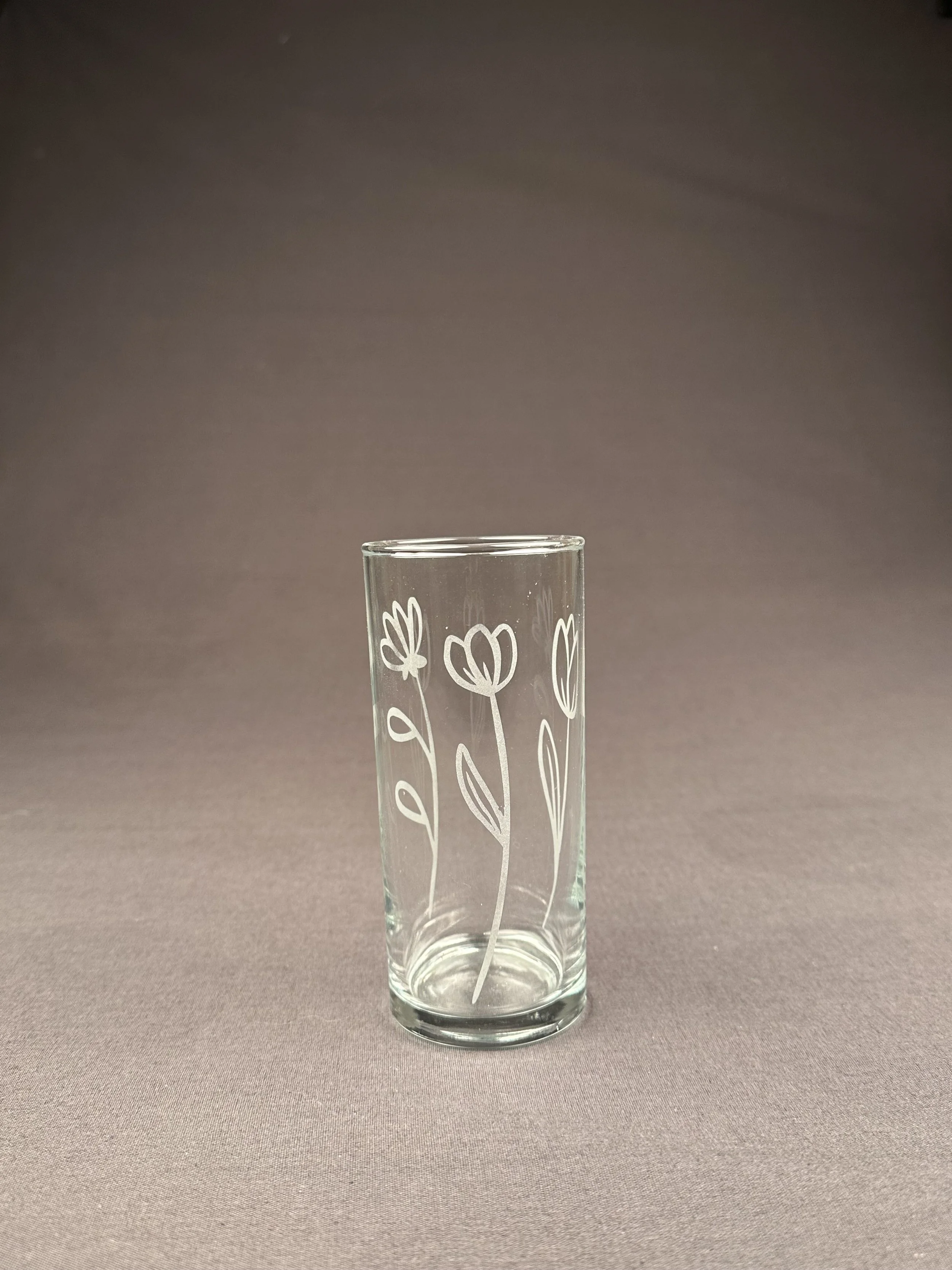 Ein durchsichtiger Glas mit weißen Blumenmustern dekoriert, auf einem neutralen Hintergrund.