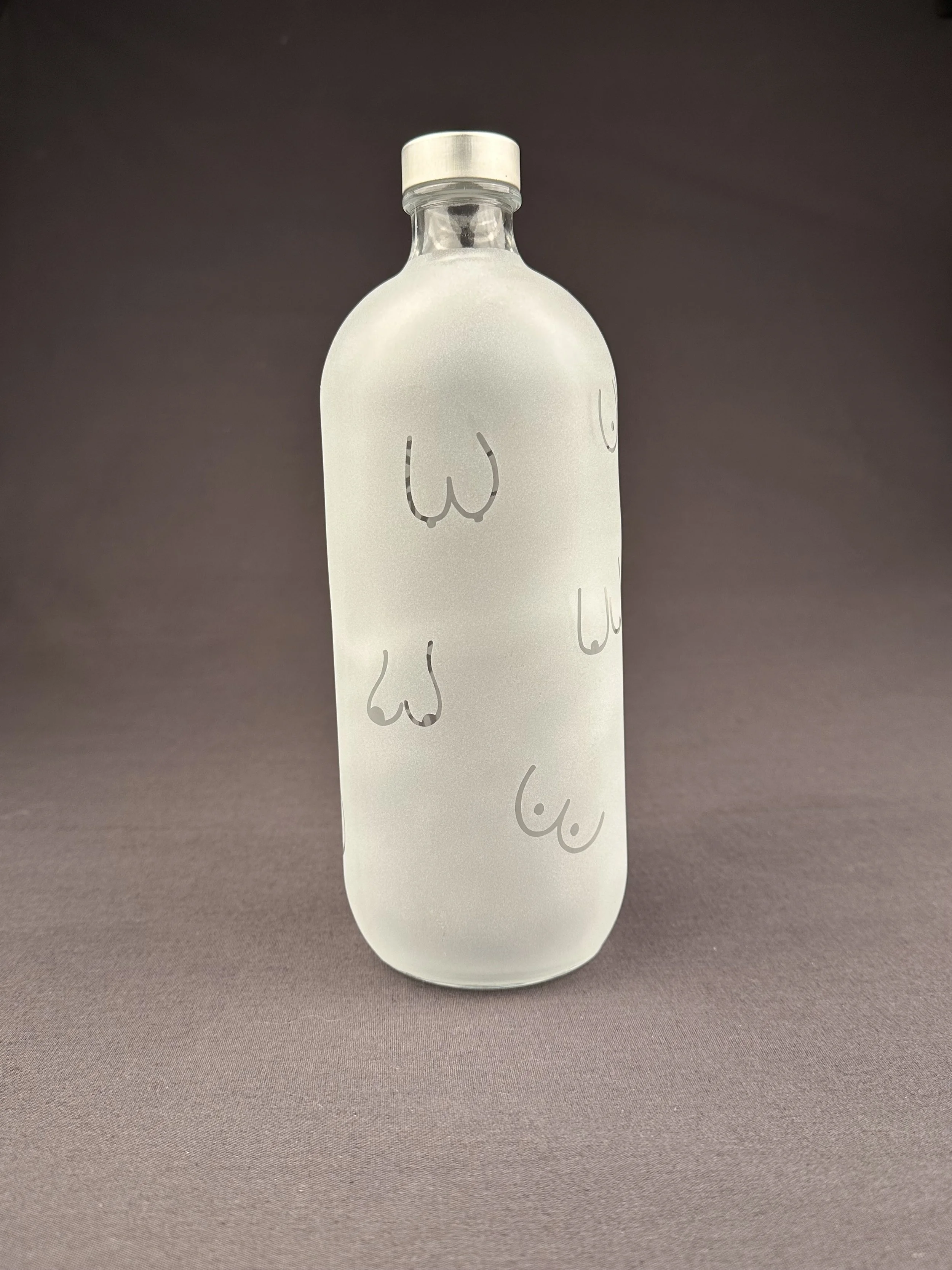 Transparente Glasflasche mit weißem Korkverschluss, verziert mit minimalistischen schwarzen Linien, die stilisierte Brustwarzen darstellen.