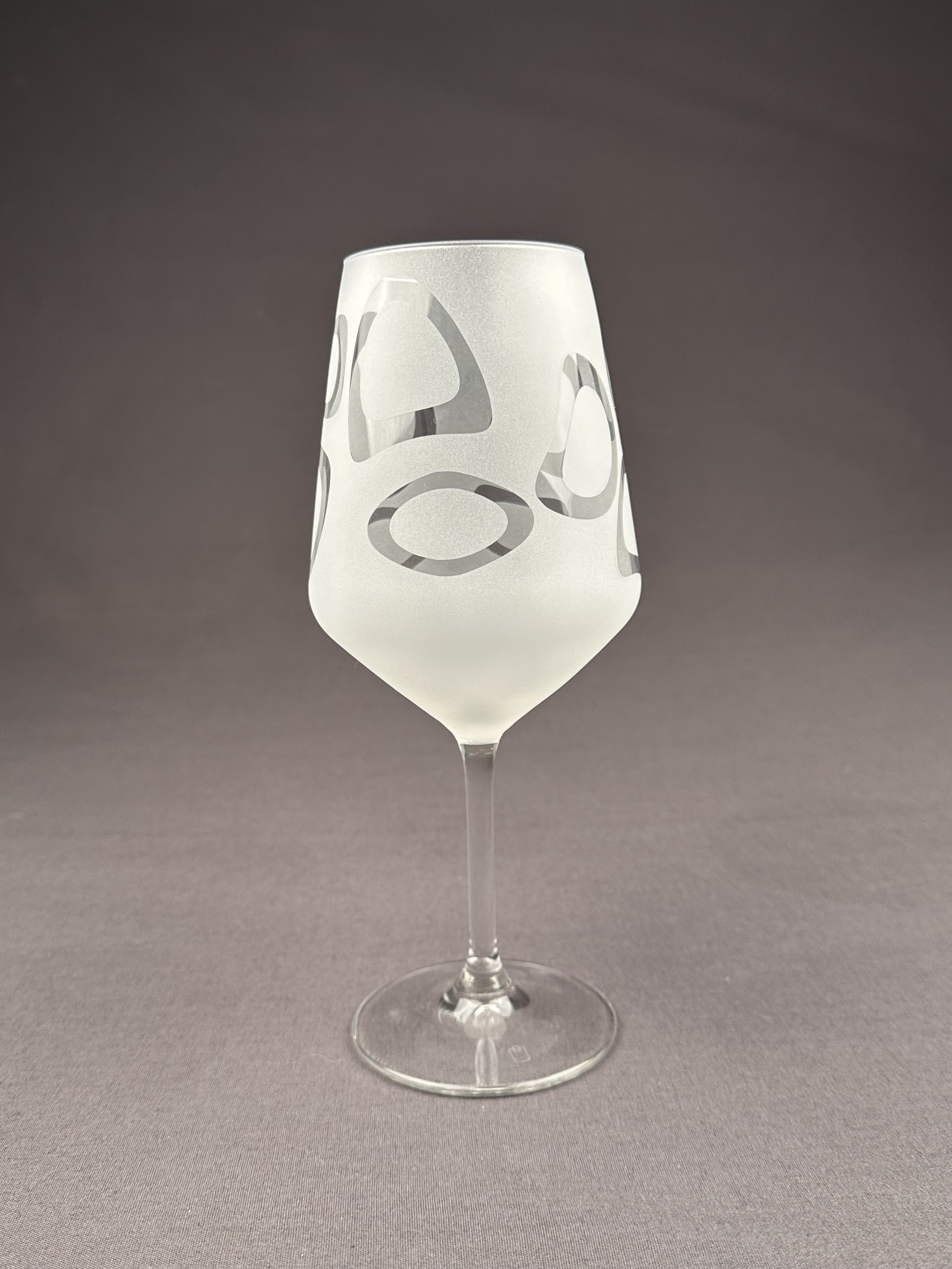 Ein durchsichtiges Weinglas mit weißen Applikationen auf grauem Hintergrund.