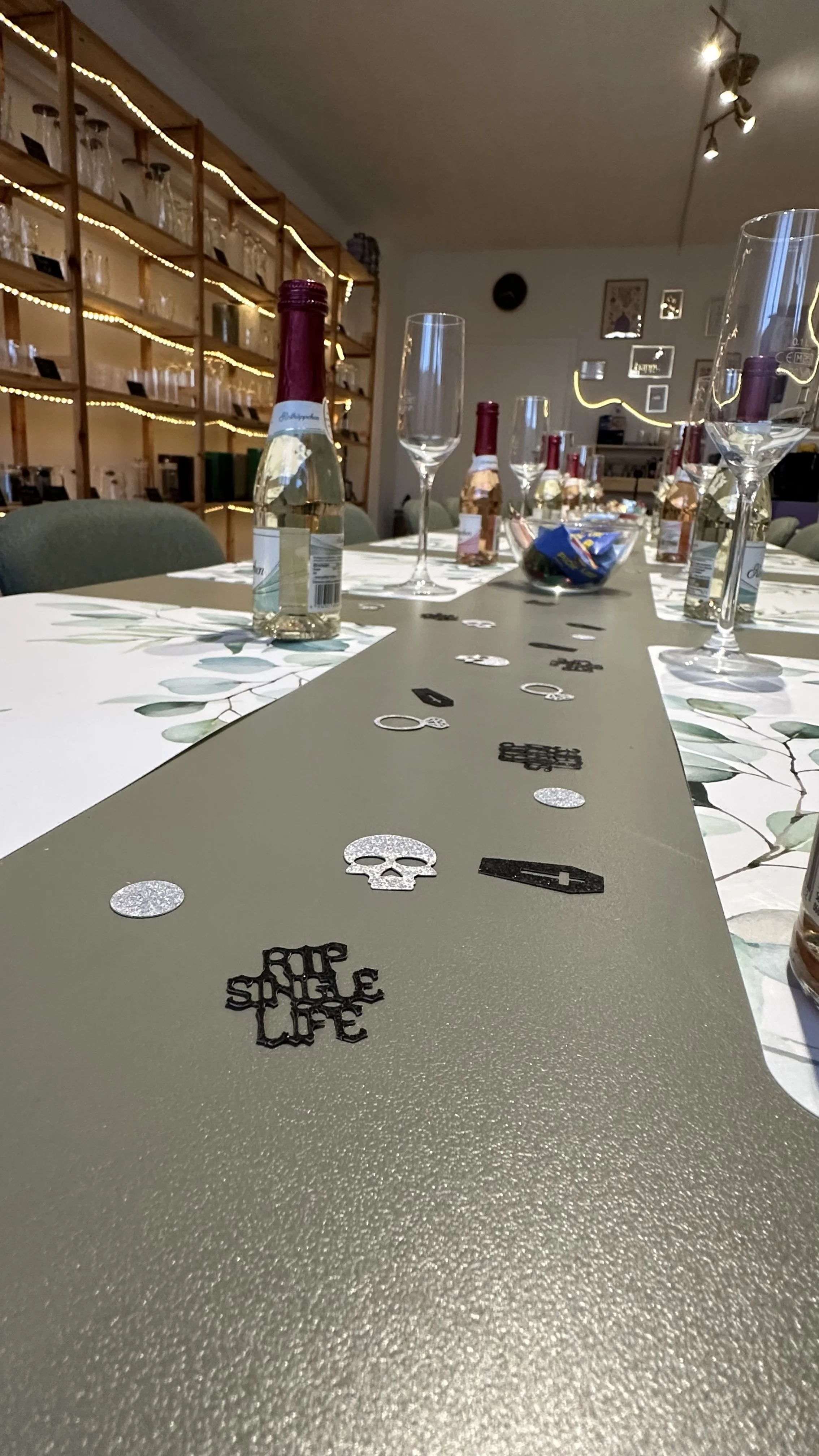 Ein festlich dekorierter Tisch mit Glasflaschen, leeren Weingläsern, eine Schüssel mit Süßigkeiten, und einem MittelsTraveller mit Silberschmuck und Kerzen in einem schön eingerichteten Raum.