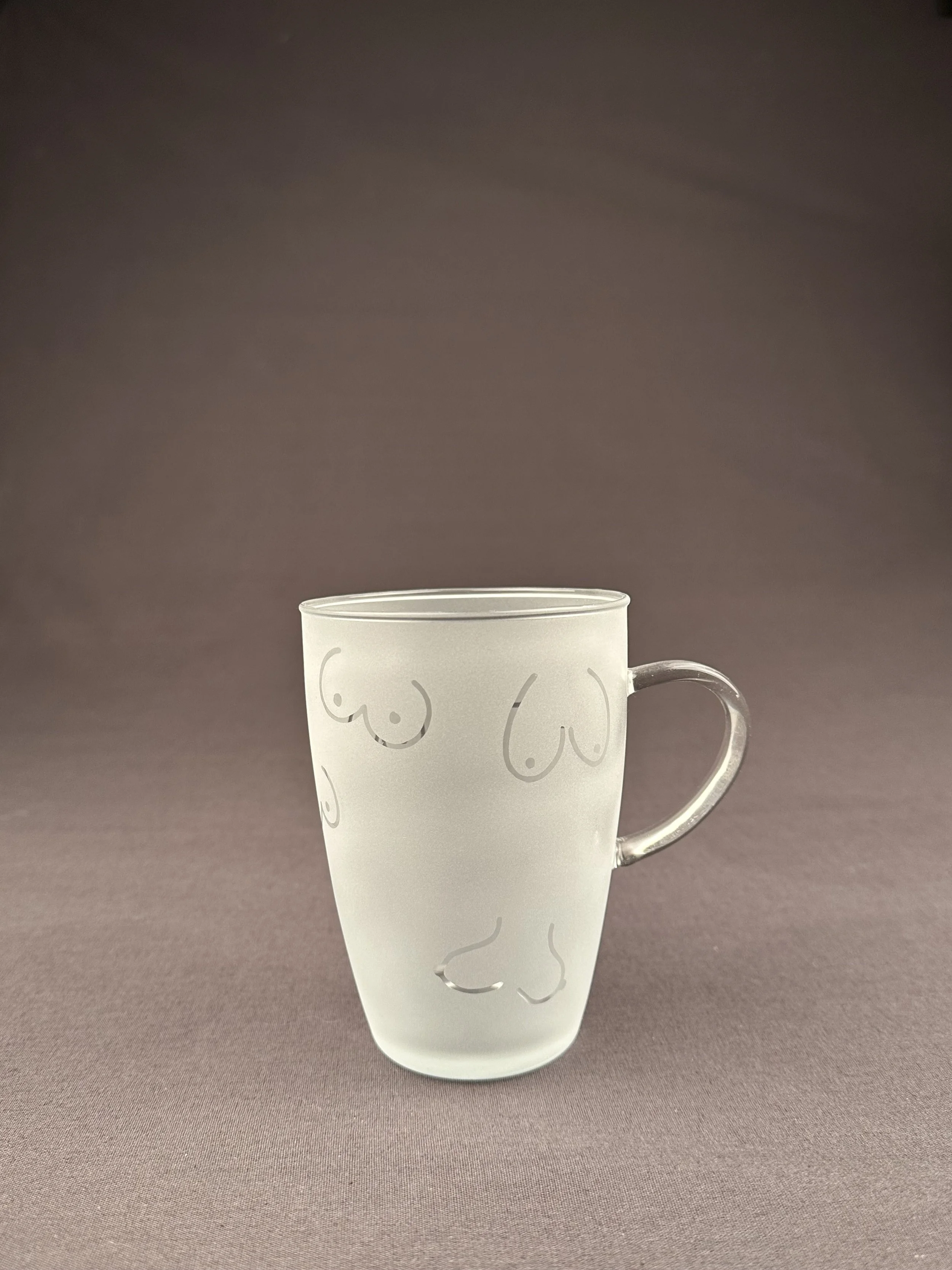 Transparenter Glas mit beruchtartigen Linien, die an Brüste und eine Nase erinnern, auf einem braunen Hintergrund.