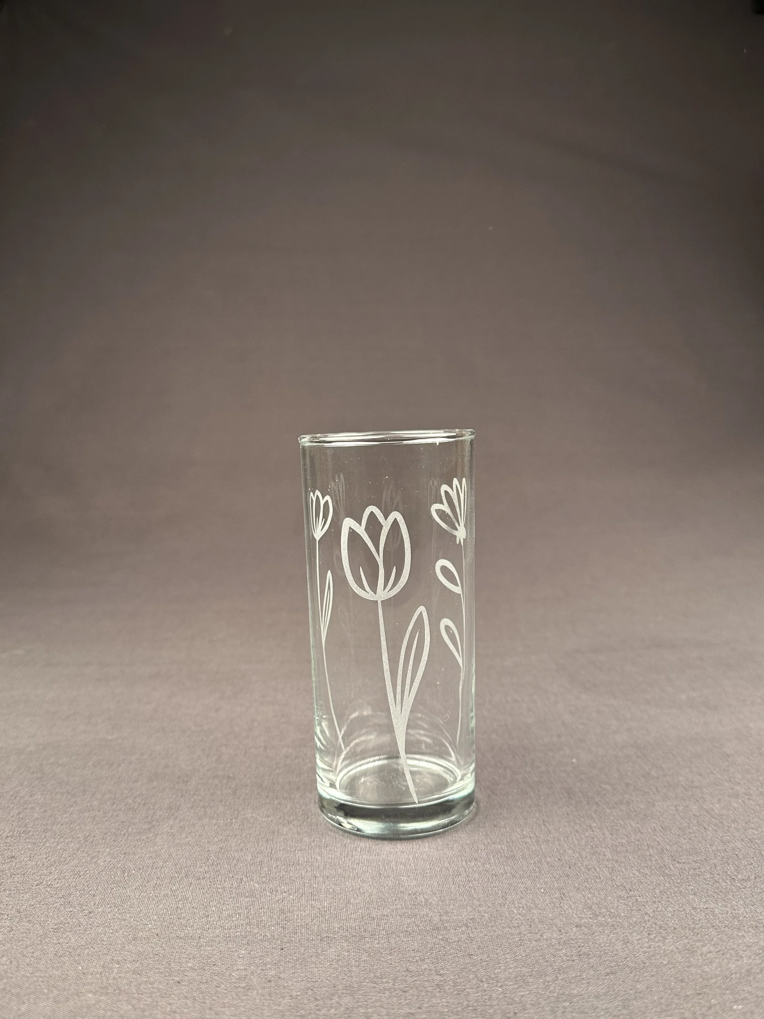 Ein transparentes Glas mit weißen Blümchenmuster, auf einem grauen Hintergrund.