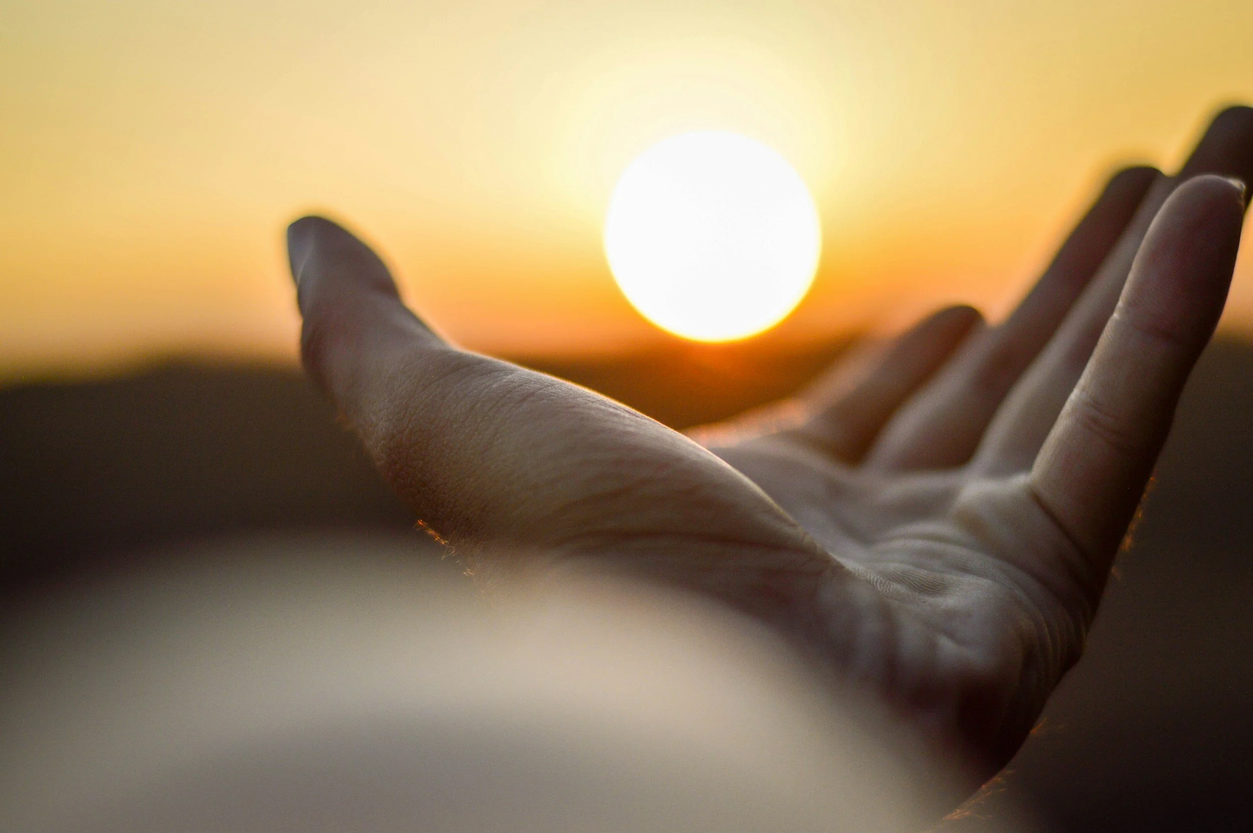 Close-up of a hand reaching out towards a setting sun during sunset.