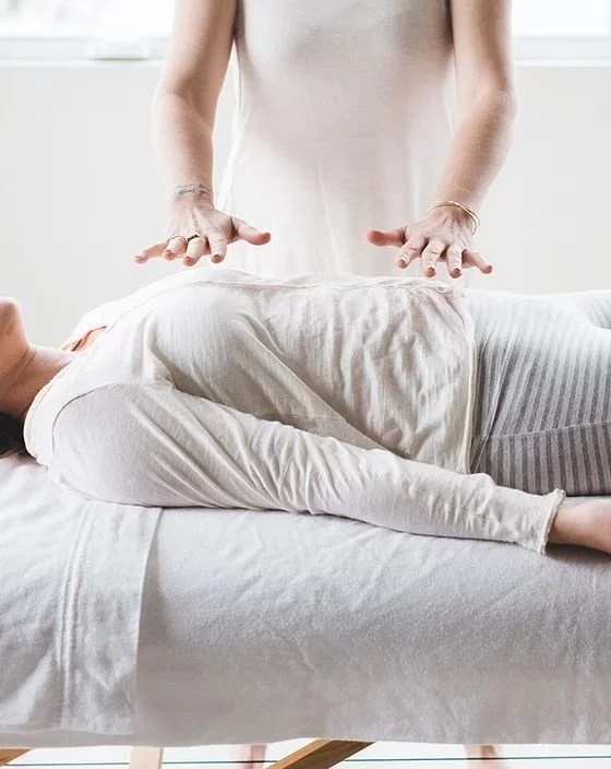Person performing reiki or energy healing on another person lying on a bed.