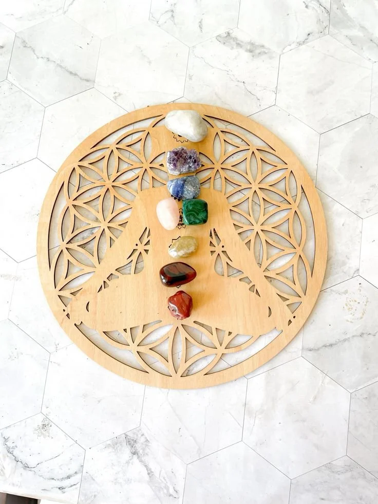 A wooden circular art piece with intricate cut-out patterns, placed on a white hexagonal tiled surface, with nine assorted crystals arranged in a vertical line on top of it.