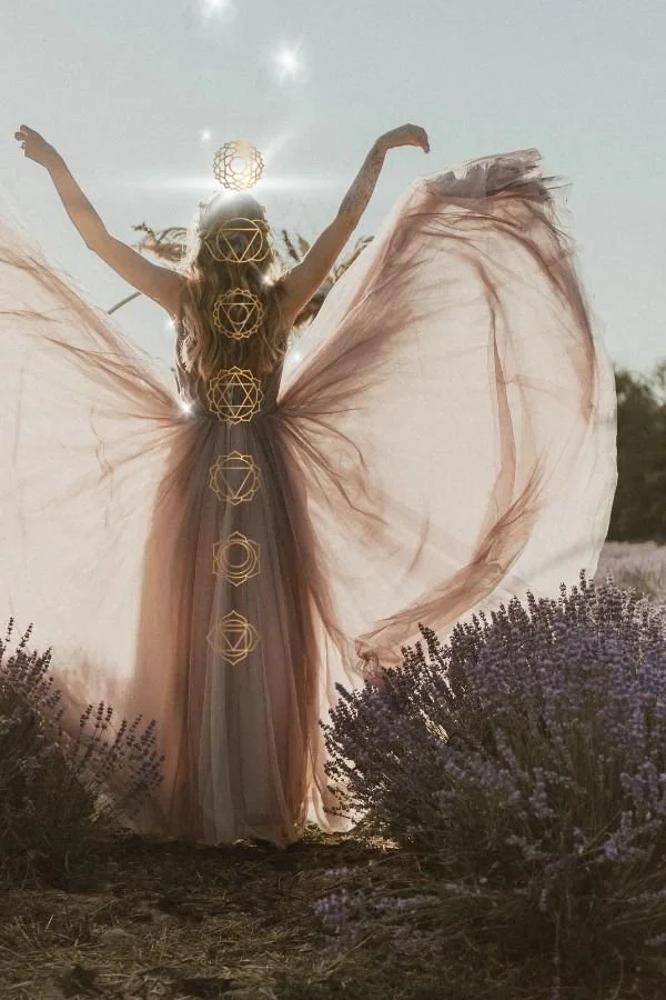 A woman in a flowing, sheer dress with large butterfly-like wings stands outdoors in a field of purple flowers. She has her arms raised, and there are glowing geometric symbols overlaying her body, with sunlight and sparkles in the sky behind her.