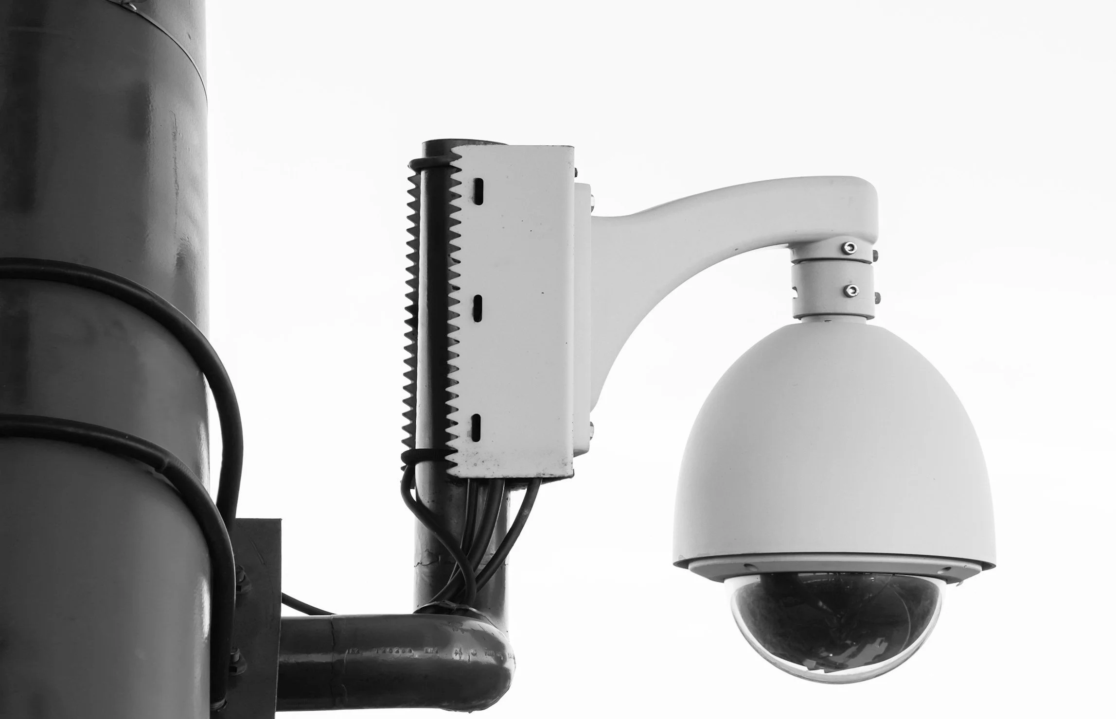 A black and white photograph of a security camera mounted on a pole.