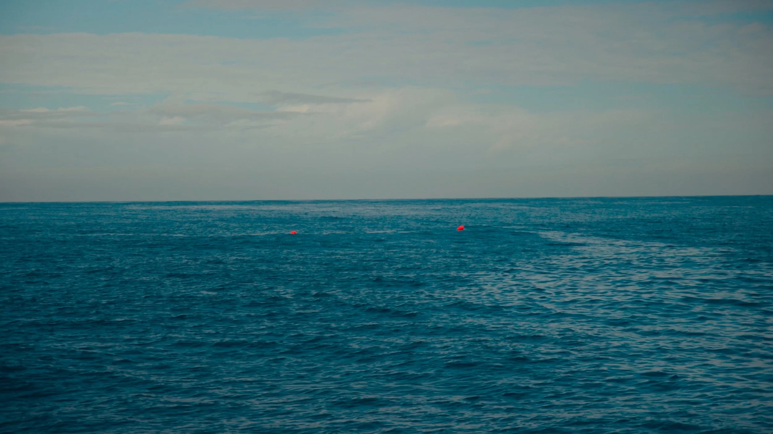Open ocean with a few red buoys and a cloudy sky