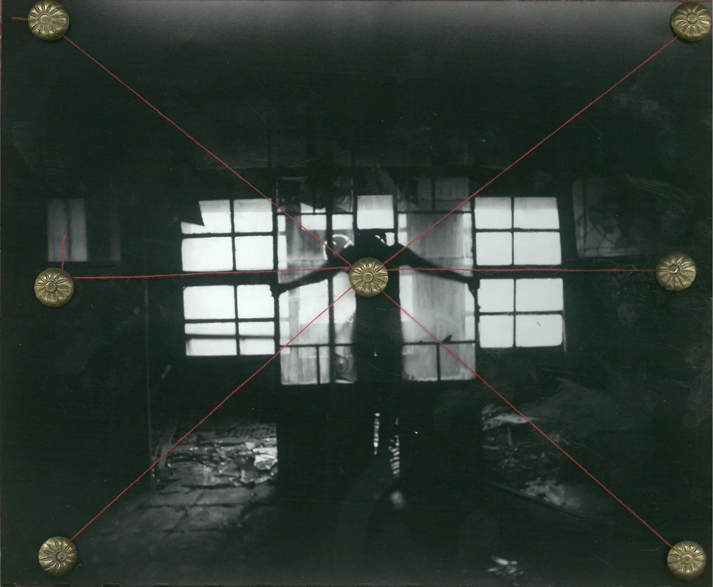A black and white photo of a person standing inside an industrial building with large windows. The person appears to be in front of the windows with light coming through, and the interior looks old and abandoned.