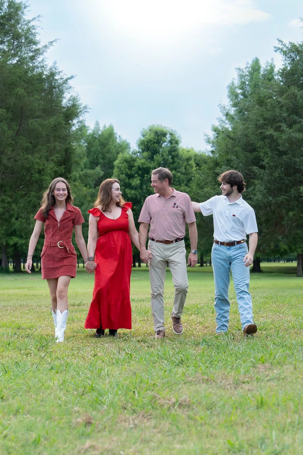 A family of four walking through a park, holding hands and smiling.