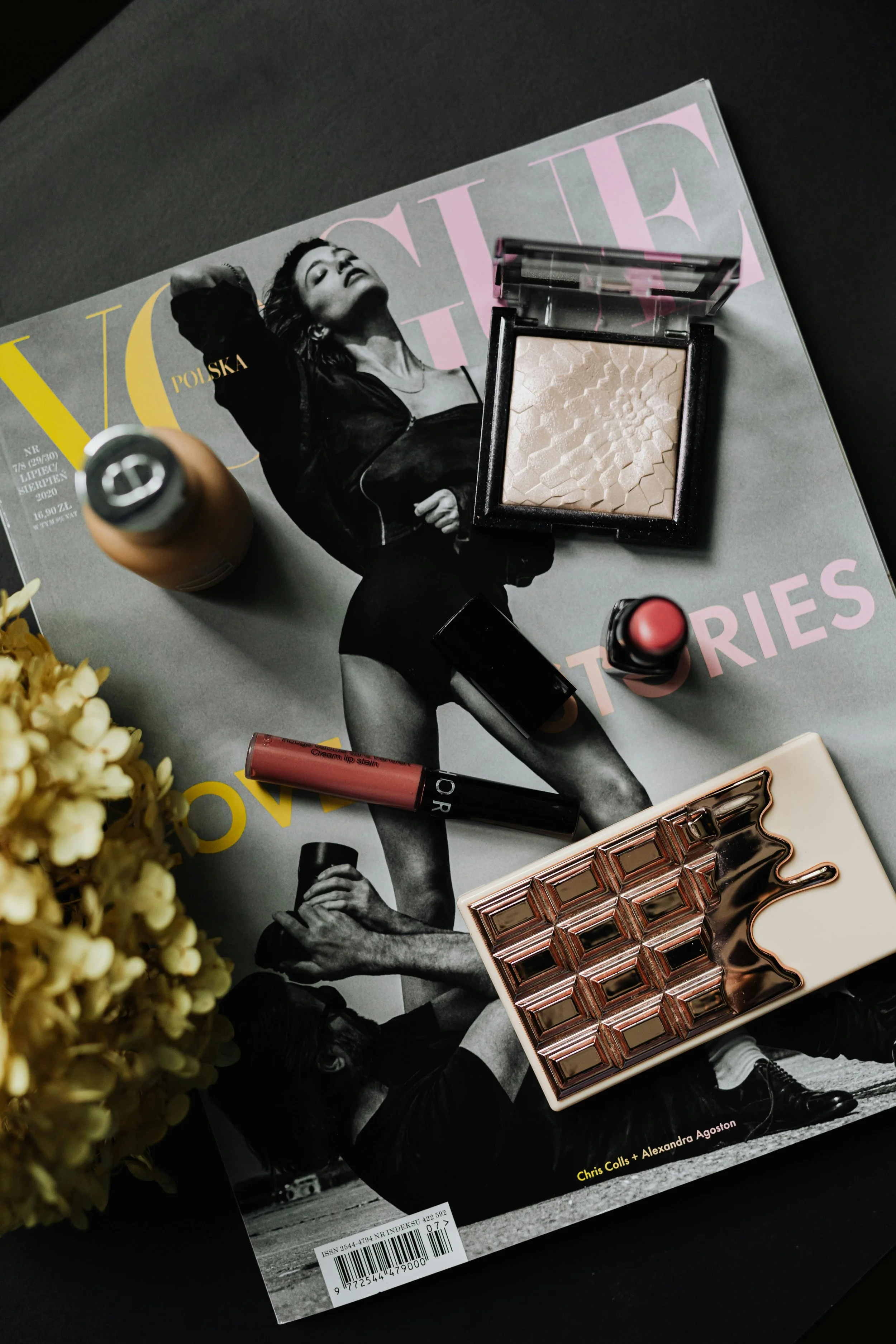 Varios productos de maquillaje sobre una revista con una mujer en la portada y un ramo de flores en el lateral izquierdo.