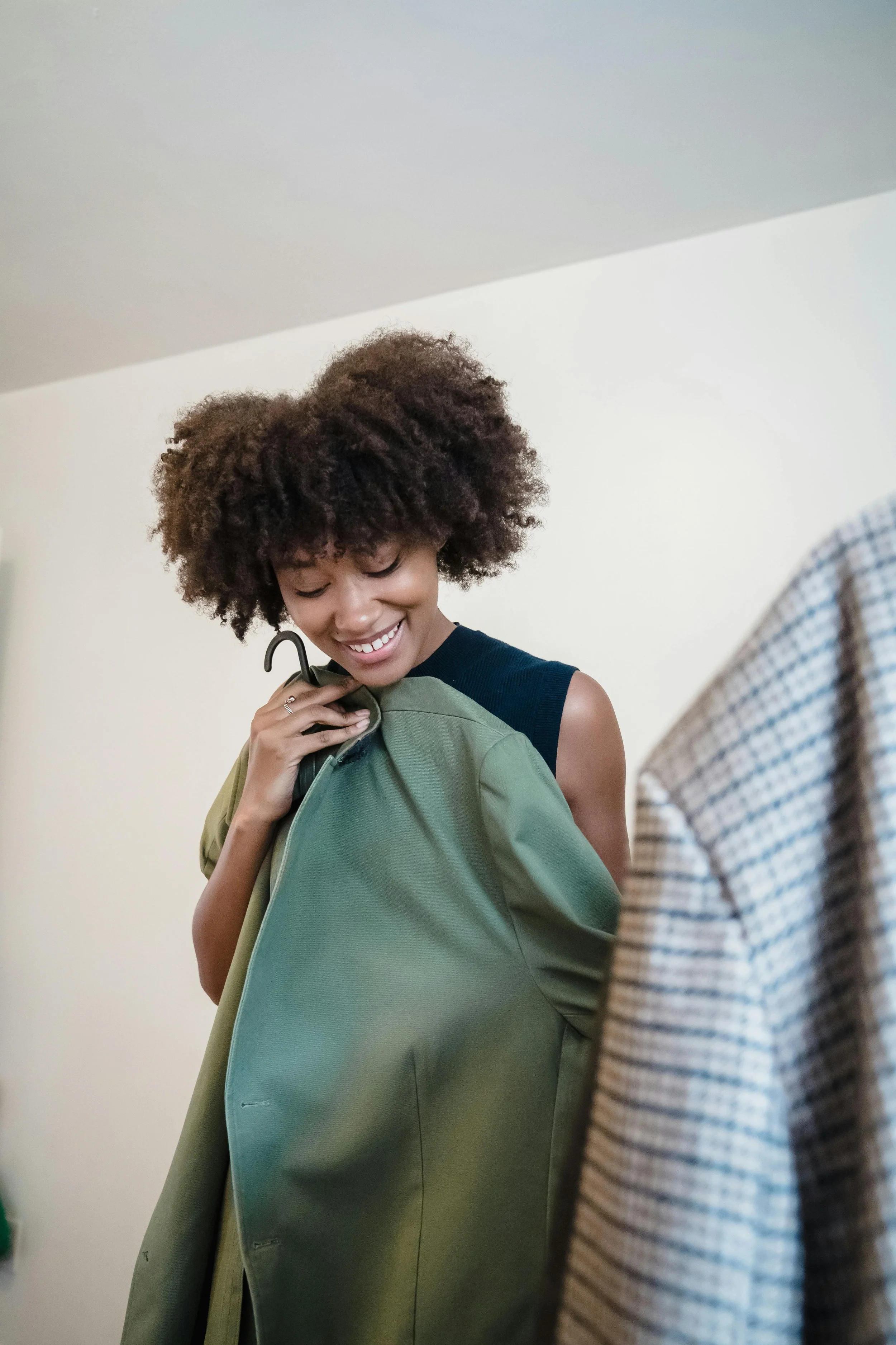 Mujer sonriente con cabello rizado, probándose un abrigo verde en una habitación