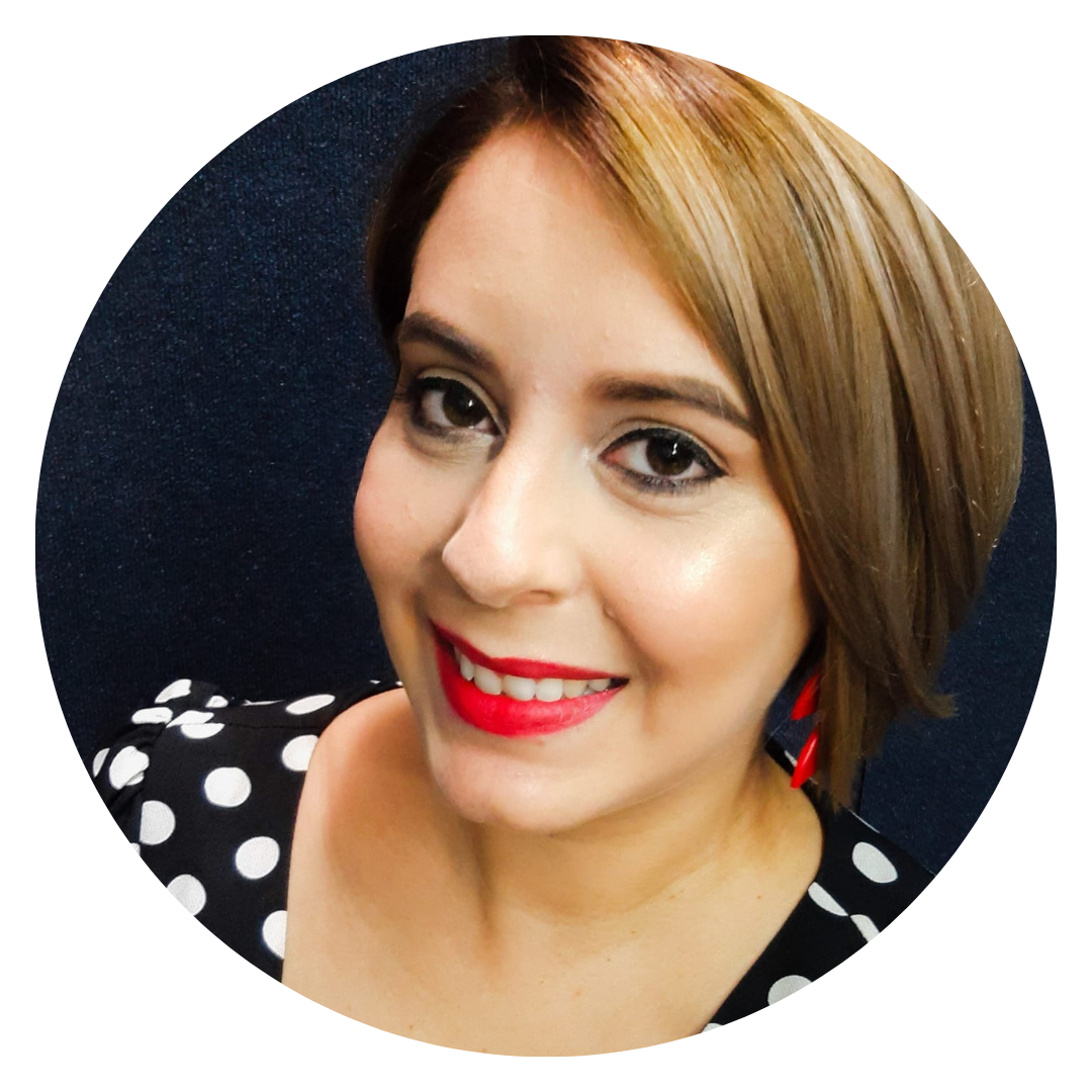 Retrato de una mujer de cabello castaño claro con corte de lado, sonrisa con labios rojos, lleva un vestido negro con puntos blancos y está en un fondo oscuro.
