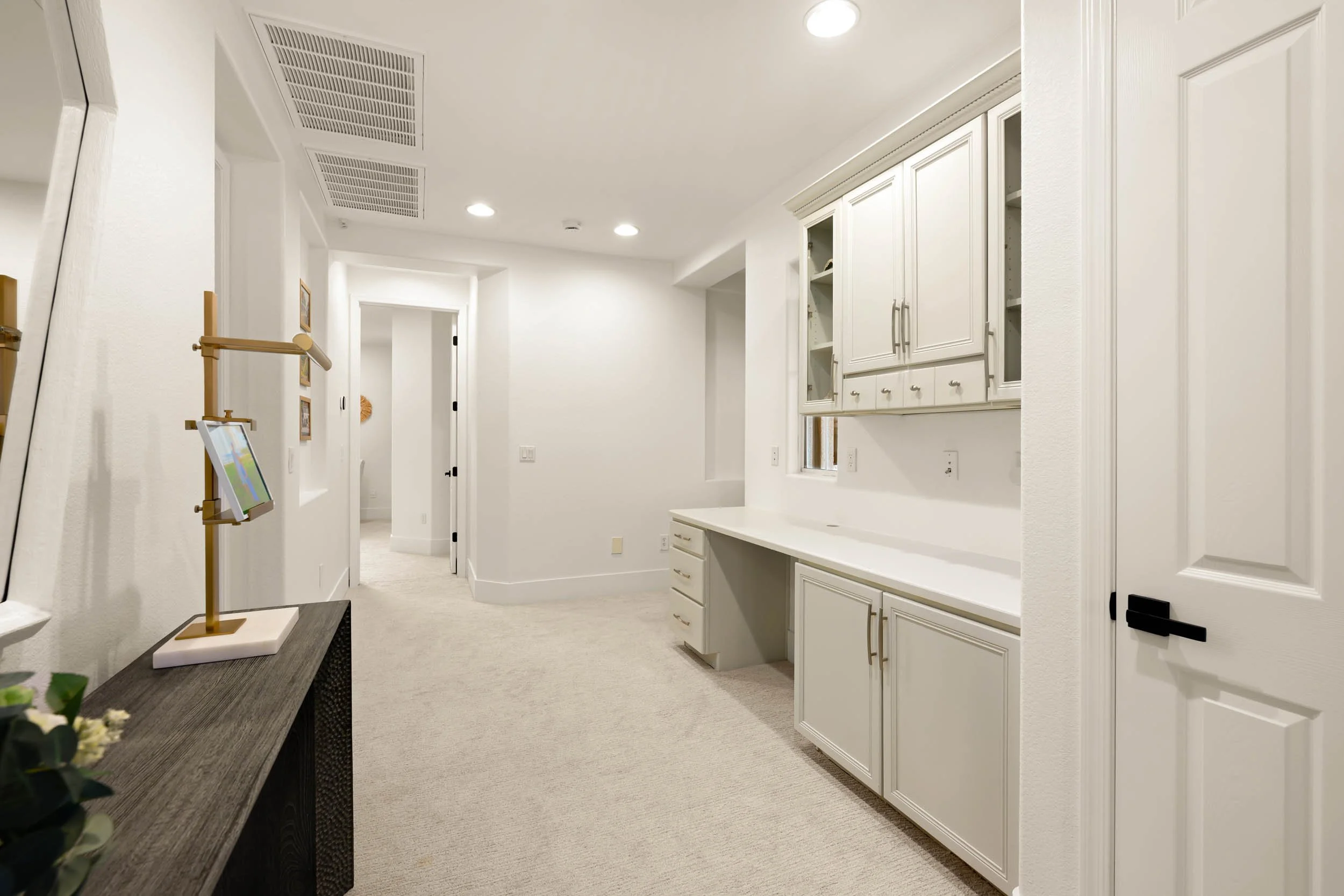 Interior view of a white kitchen or utility room with white cabinets, a built-in desk area, and soft ceiling lighting.