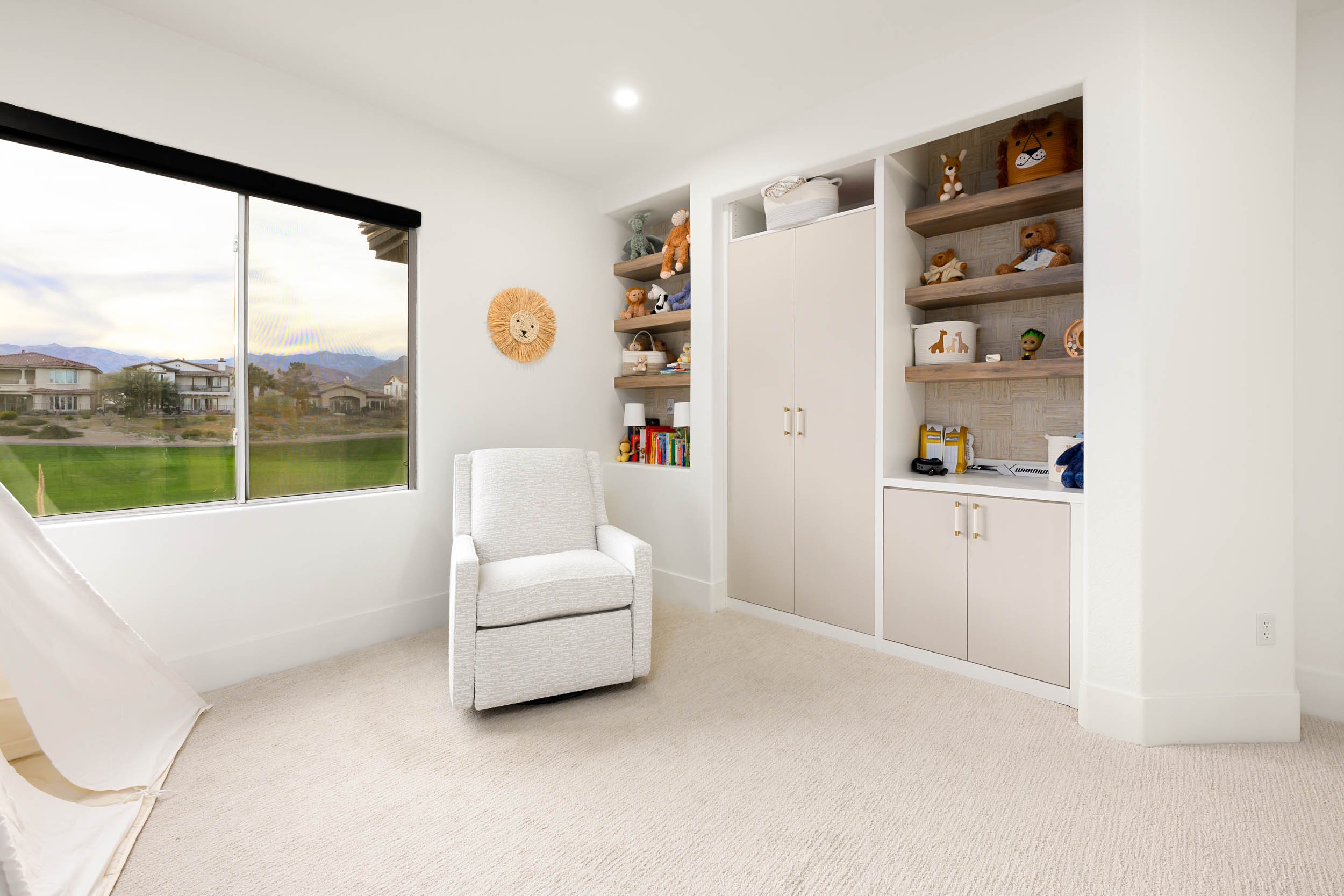 Bright children's room with a large window, white armchair, and built-in shelves filled with stuffed animals and books.