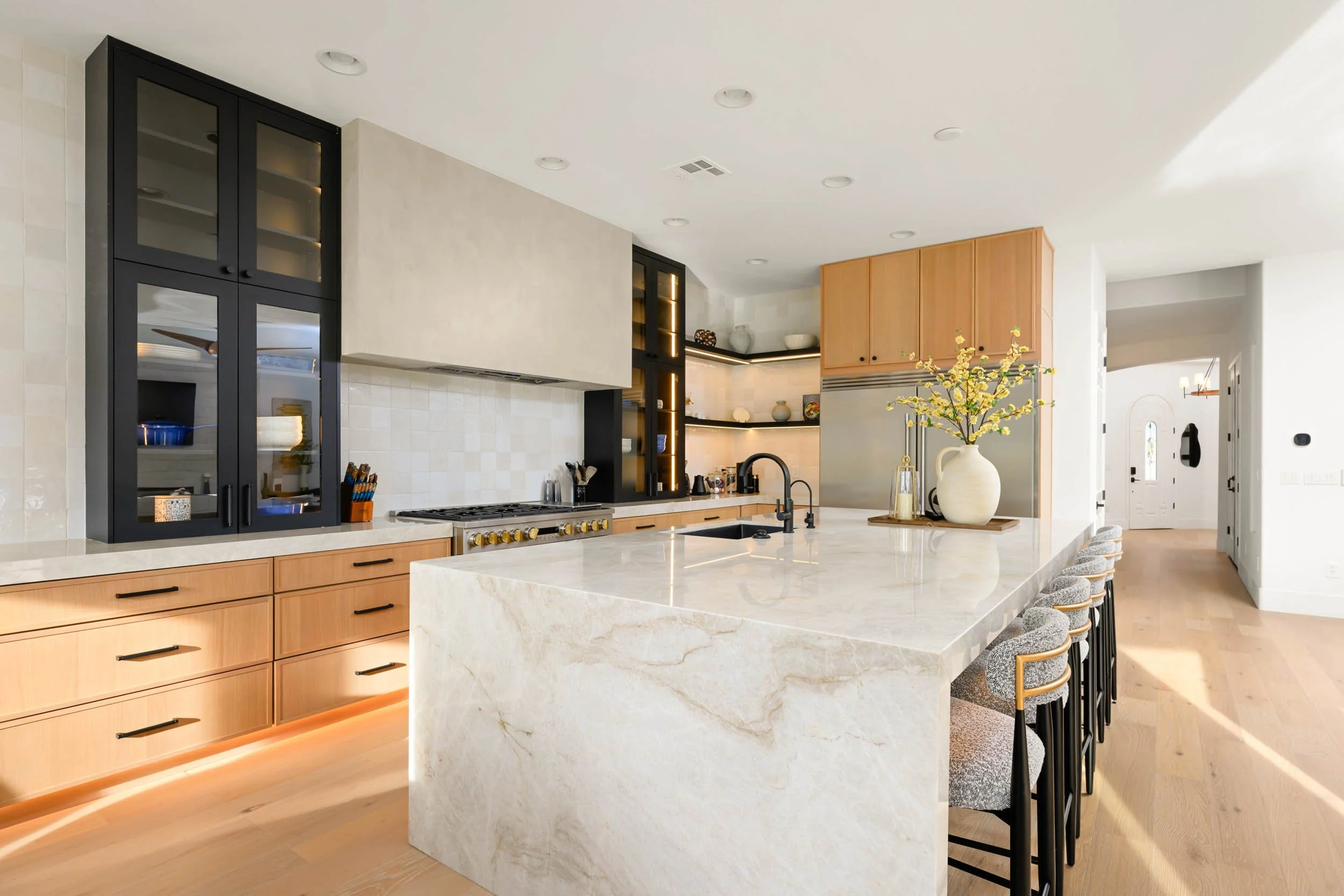 Modern kitchen with a large marble island, black cabinetry, and open wooden shelves with decorative dishes and vases.